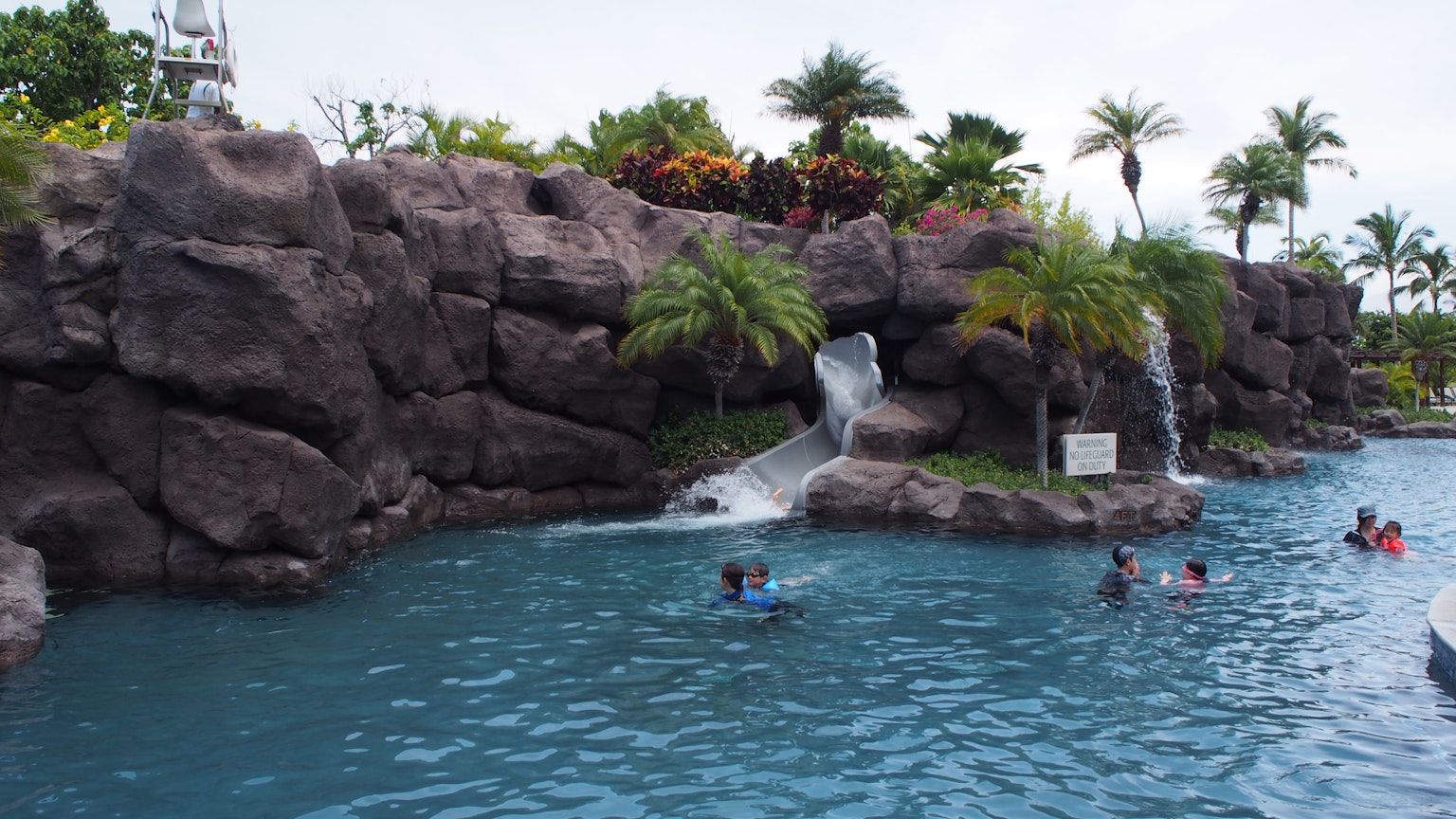Scena di resort con piscina blu e cascata con persone che si divertono nell'acqua