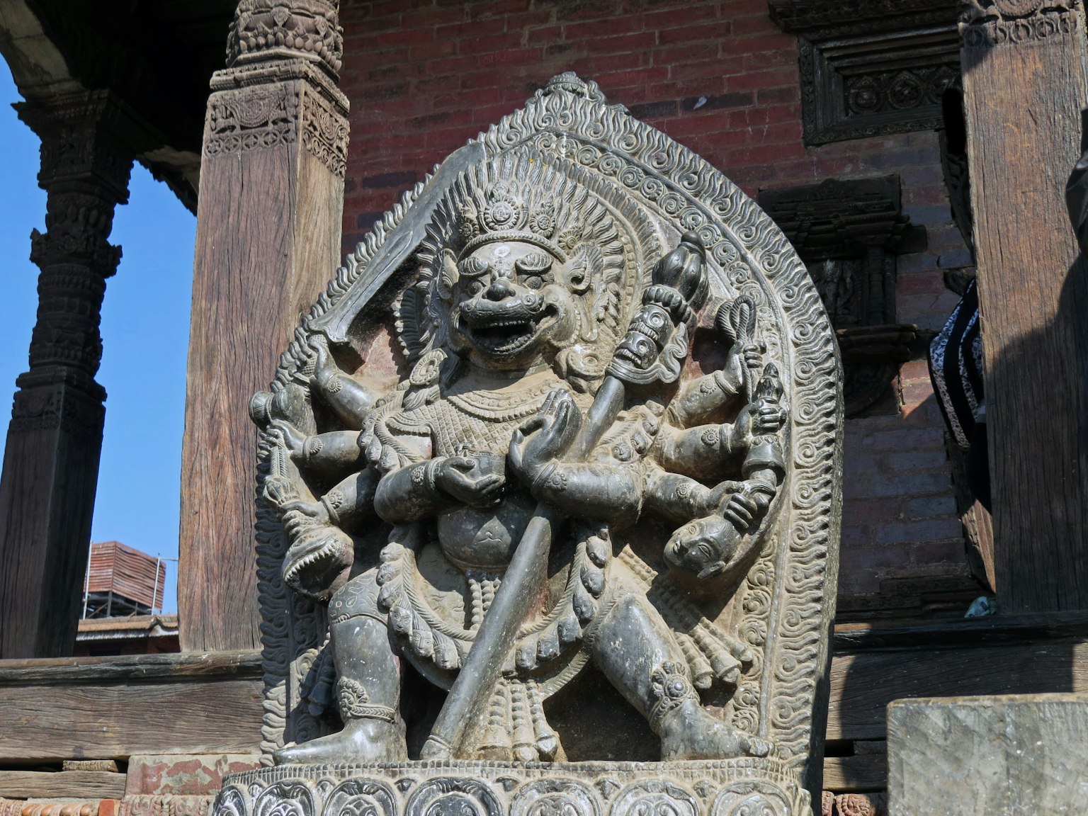 Scultura in pietra di una divinità a più braccia con cielo blu sullo sfondo