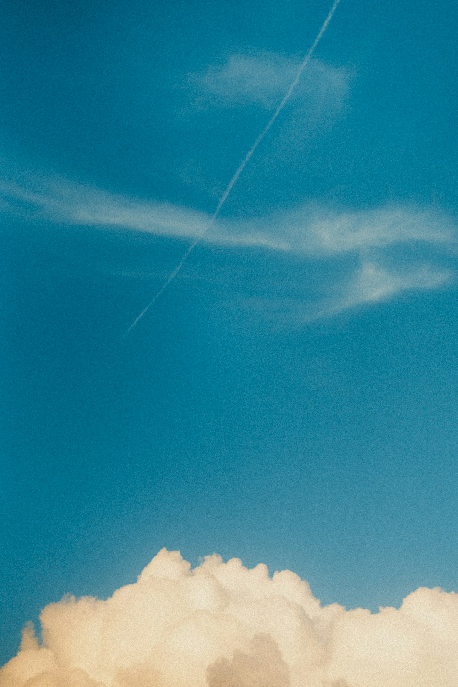 White clouds against a clear blue sky with a contrail