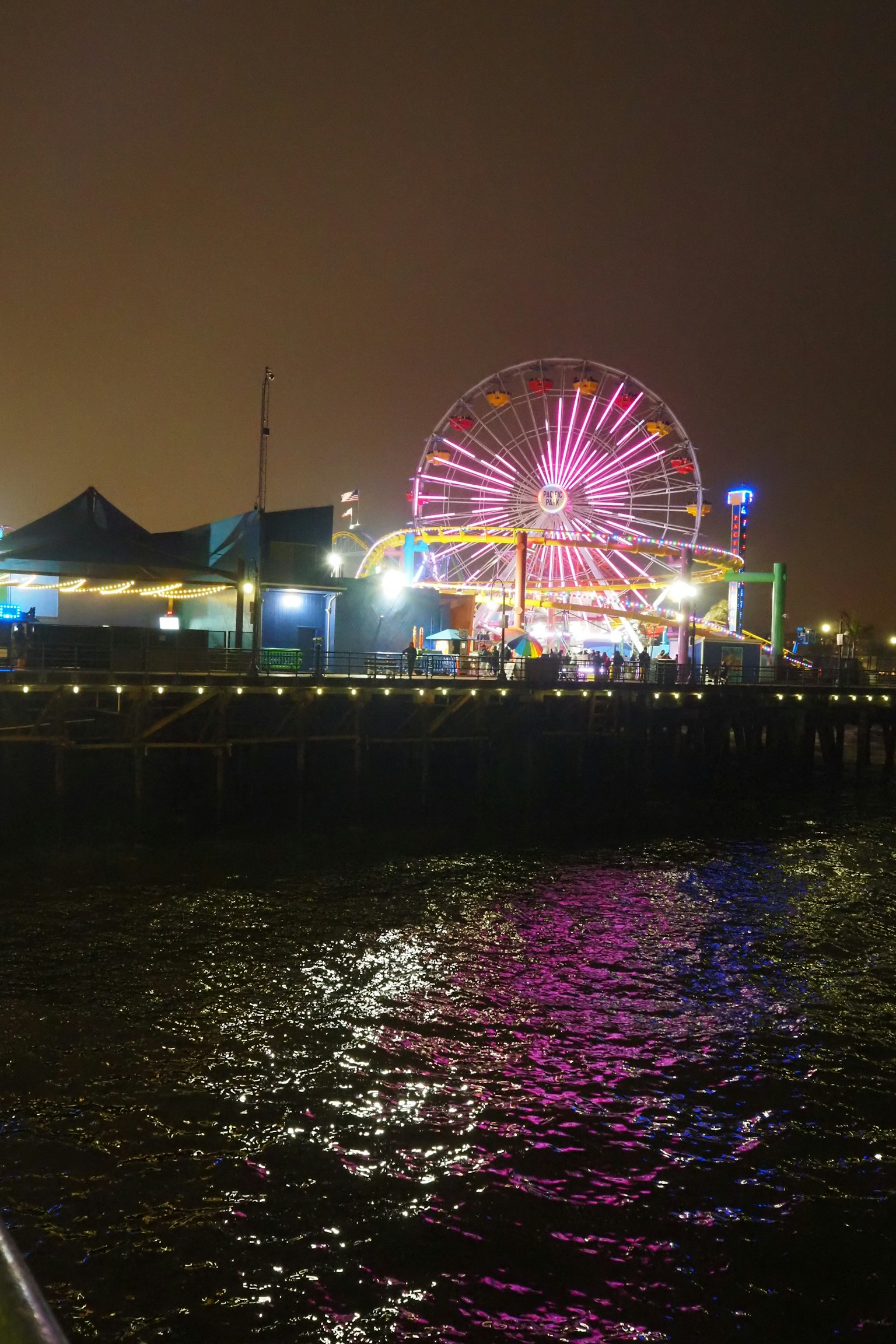 Grande roue colorée et lumières vives se reflétant sur l'eau la nuit