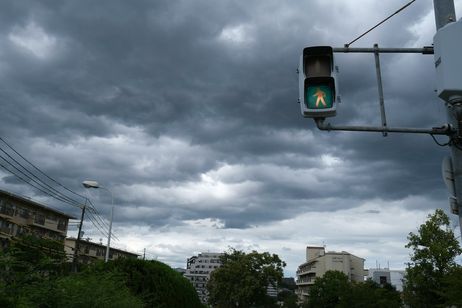 Lampu lalu lintas hijau menyala di bawah langit mendung dengan bangunan di sekitarnya