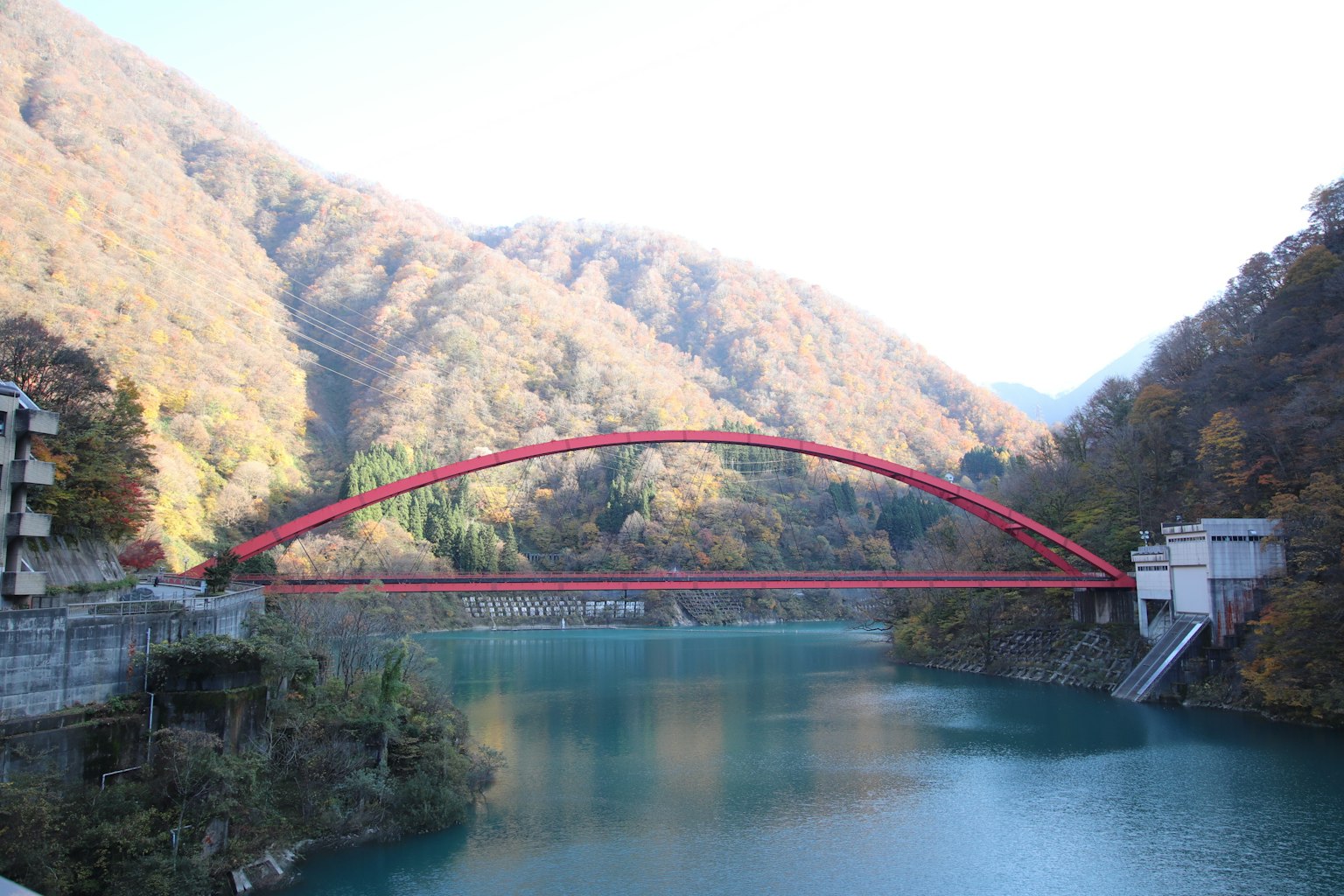 Jembatan lengkung merah di atas danau tenang dikelilingi pegunungan musim gugur