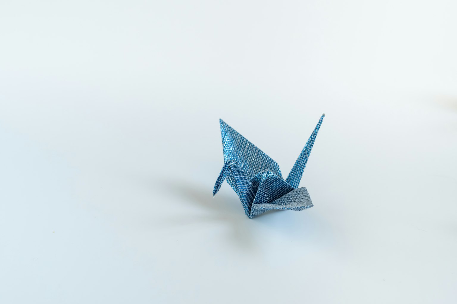 Une grue en origami bleue placée sur un fond blanc