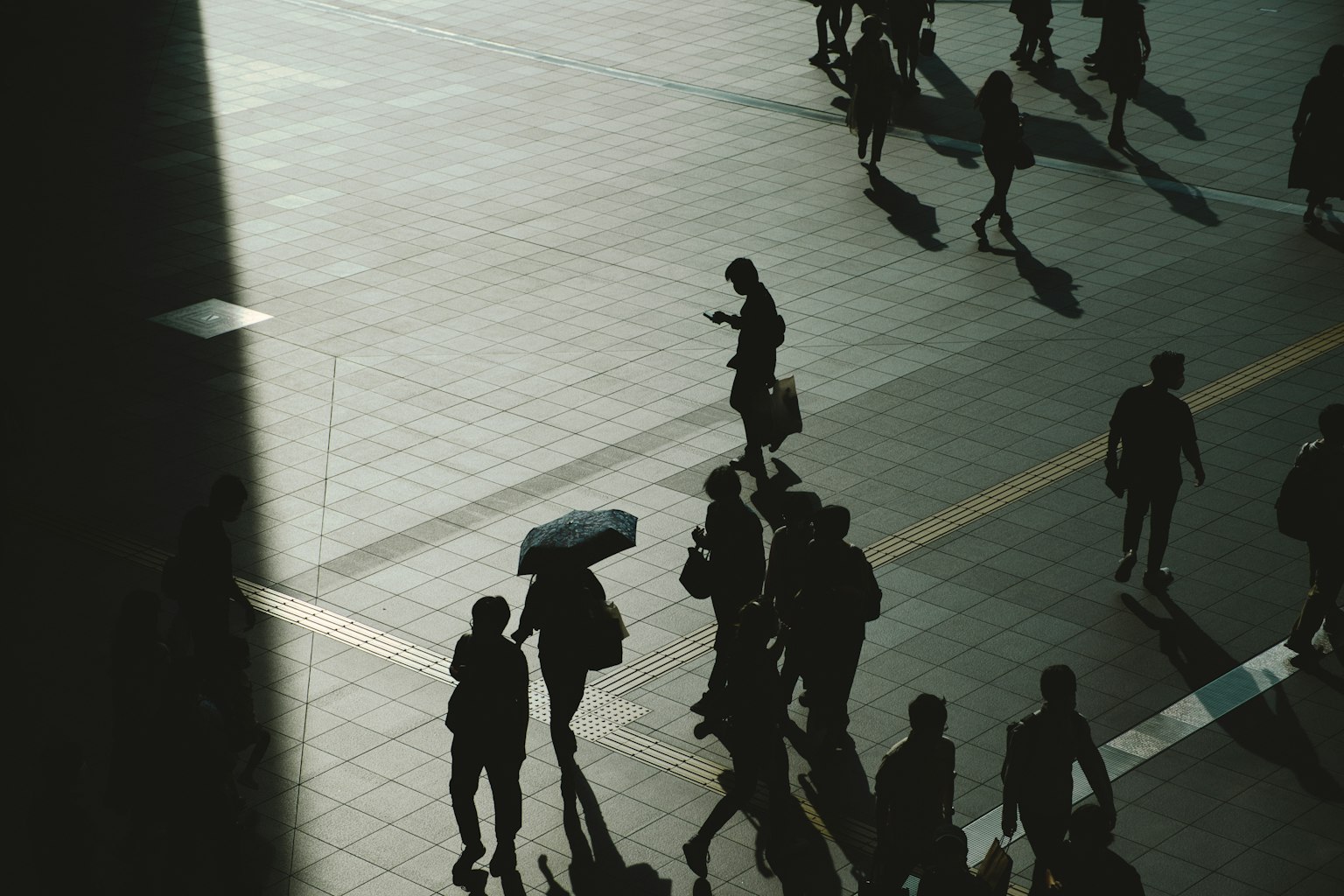 Escena urbana con personas caminando y sombras largas proyectadas en el suelo