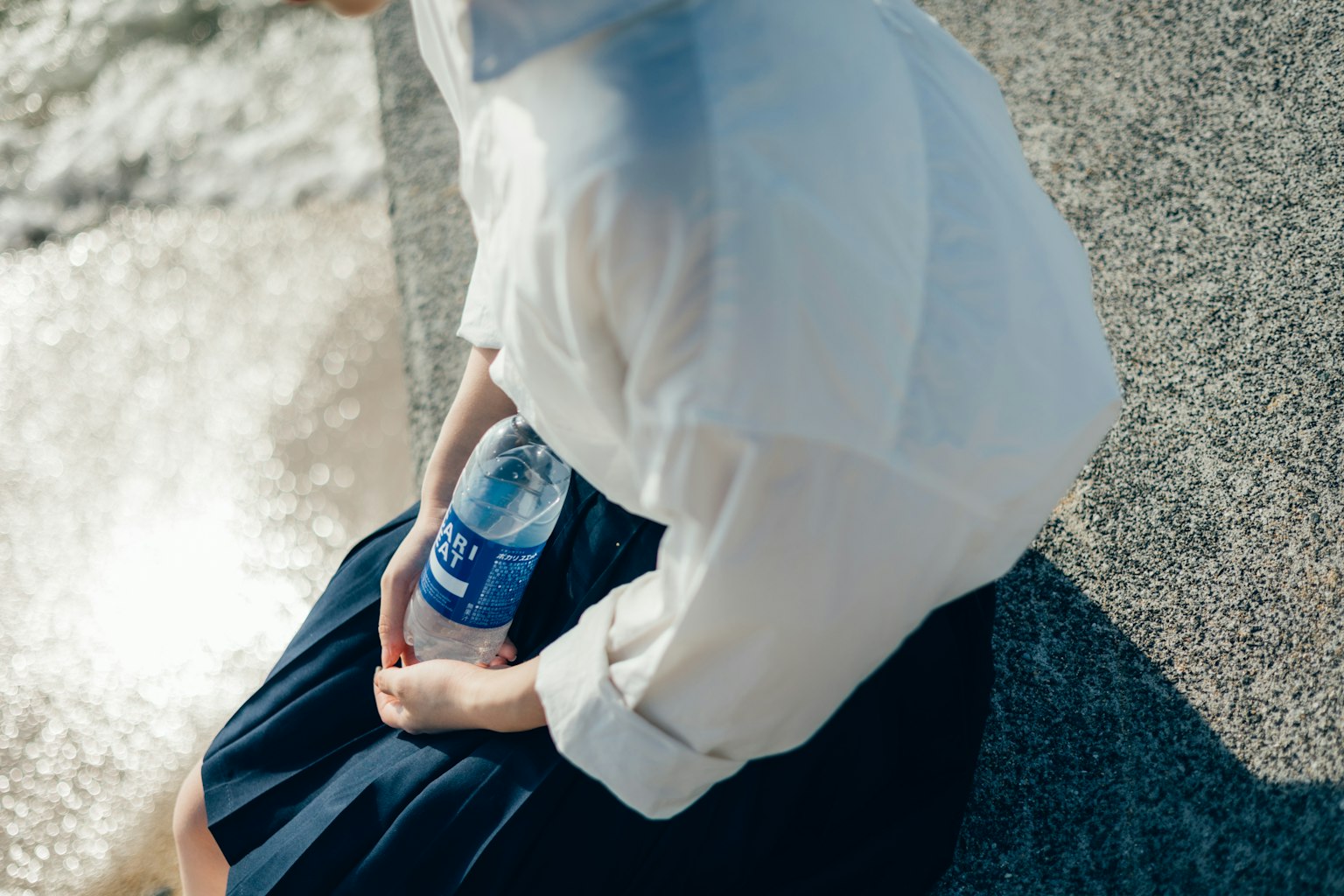 Personne portant une chemise blanche assise près de l'eau tenant une bouteille