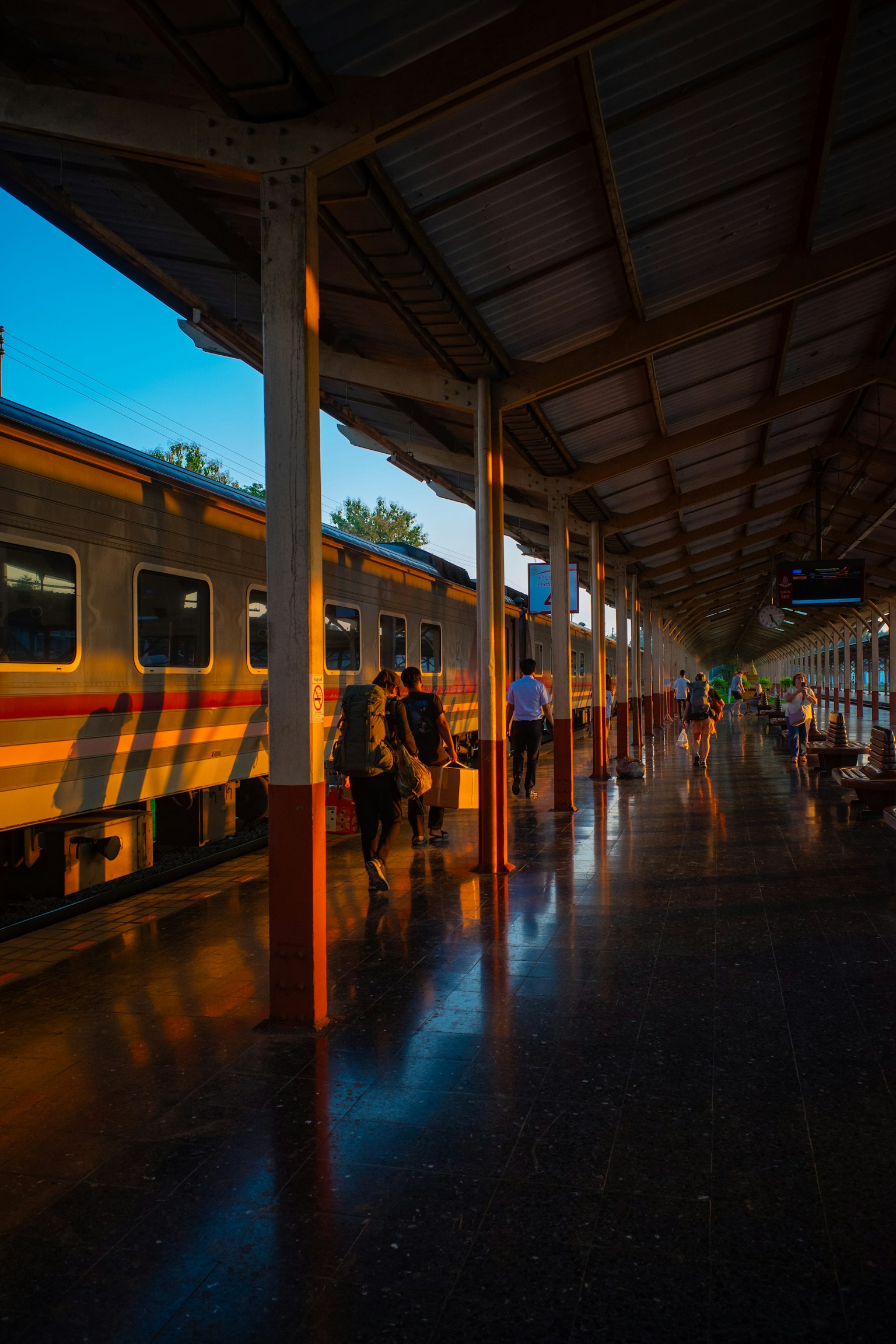 A sunset scene at a train station with passengers and a train