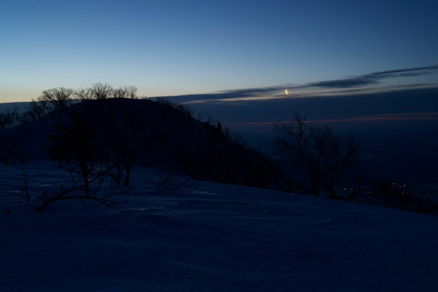 Schneebedeckter Hügel bei Dämmerung mit dem Mond am Himmel