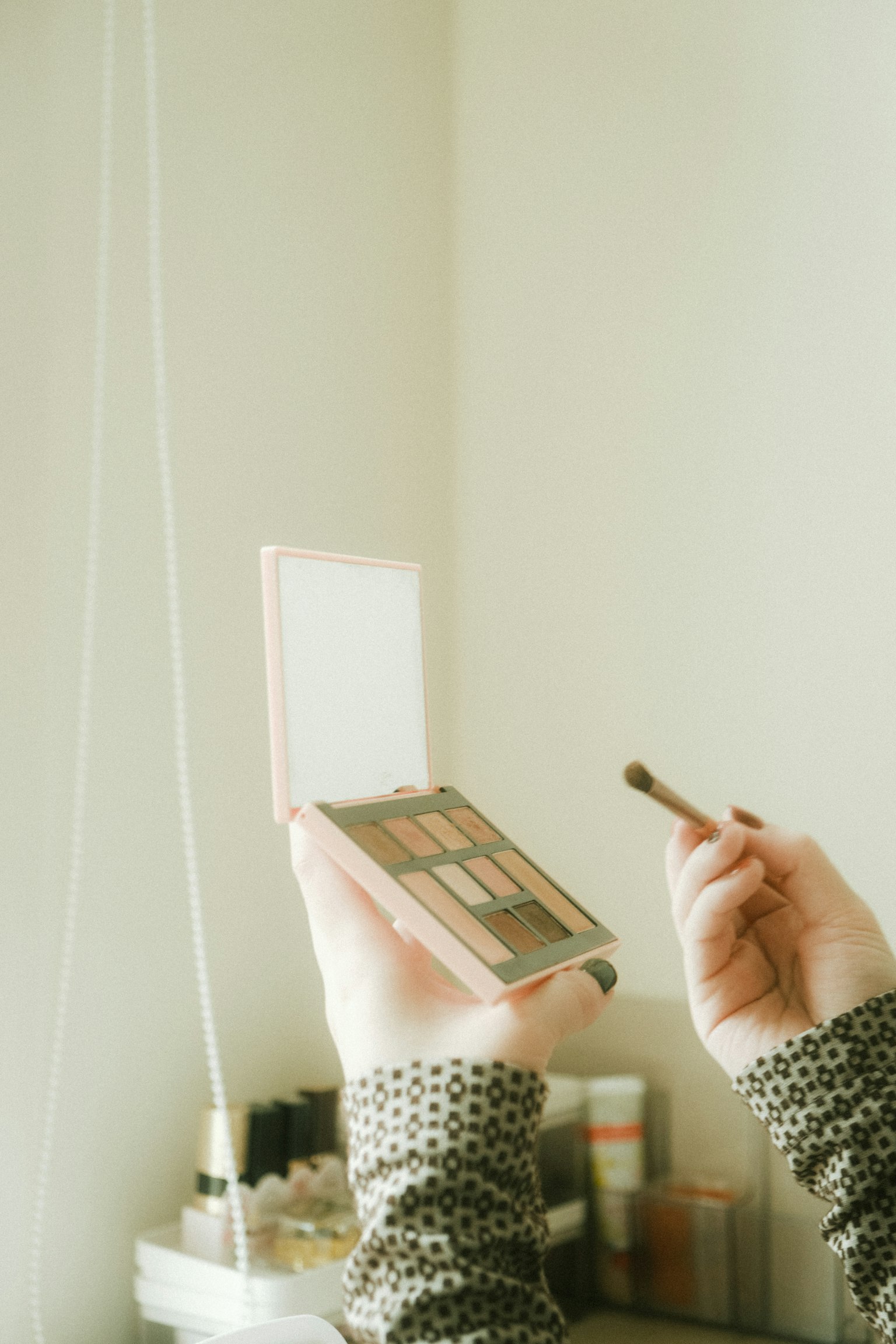 手にアイシャドウパレットを持つ女性の手とメイクブラシの画像