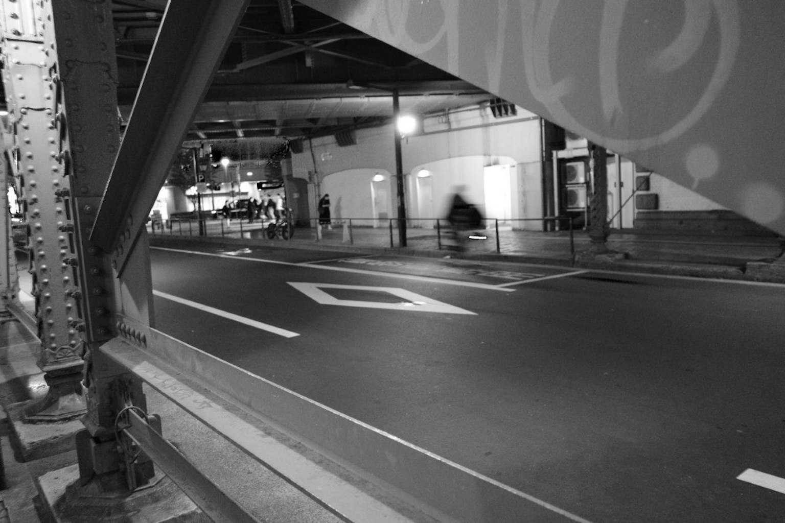 Schwarz-Weiß-Stadtansicht mit einer Straße unter einer Brücke und einem Passanten