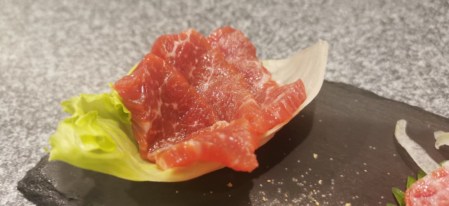 Irisan daging segar di atas daun selada