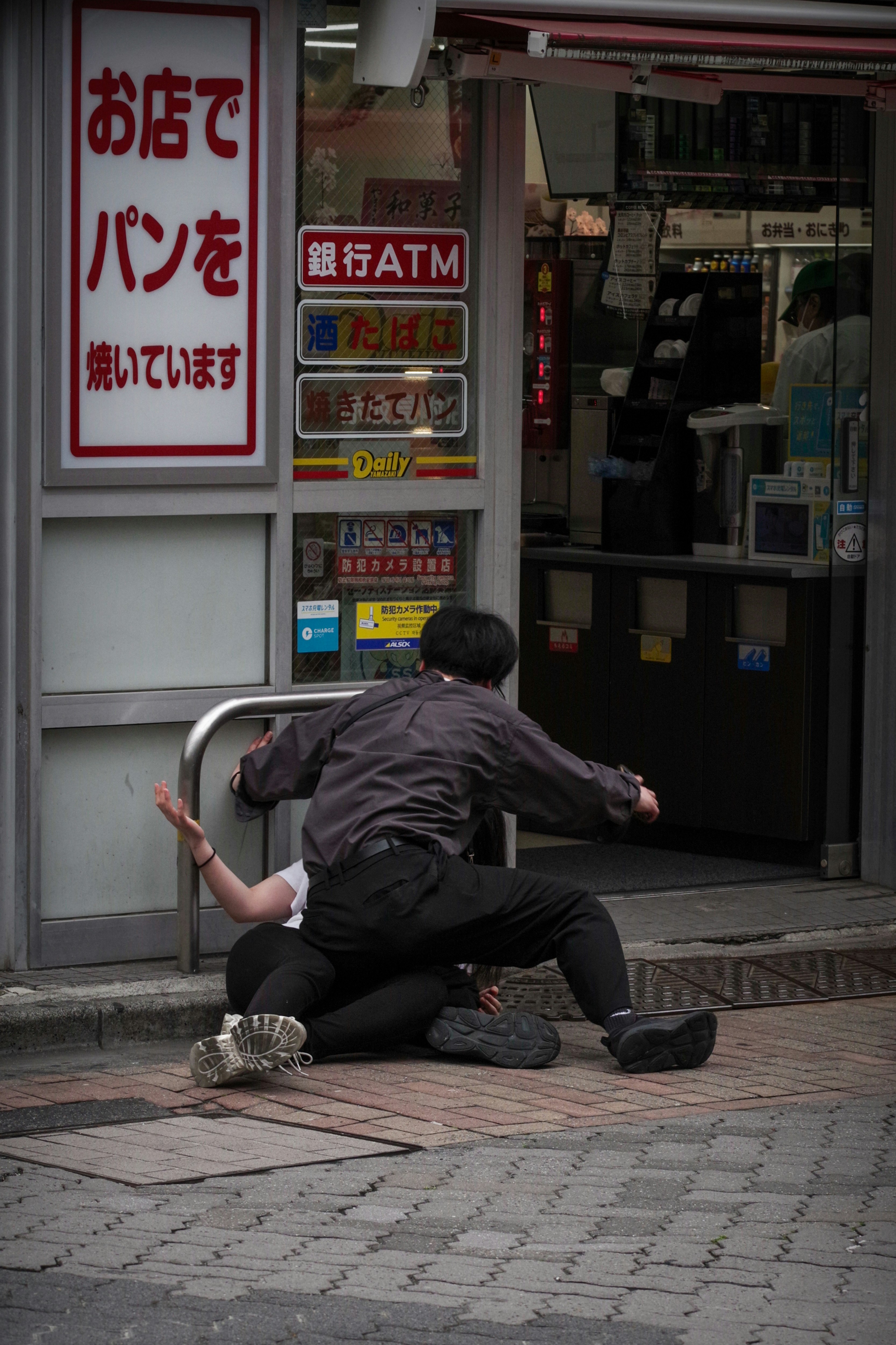 路地の店先にあるATM前で座り込む人