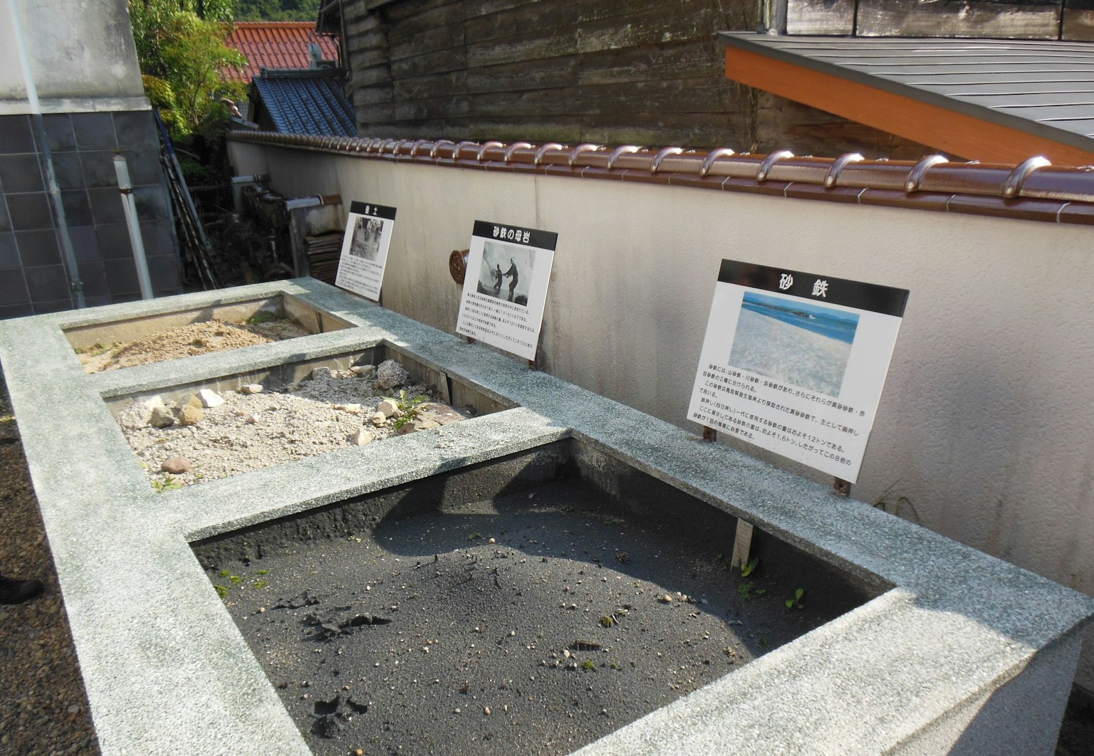 Area pameran luar dengan papan informasi dan dasar batu