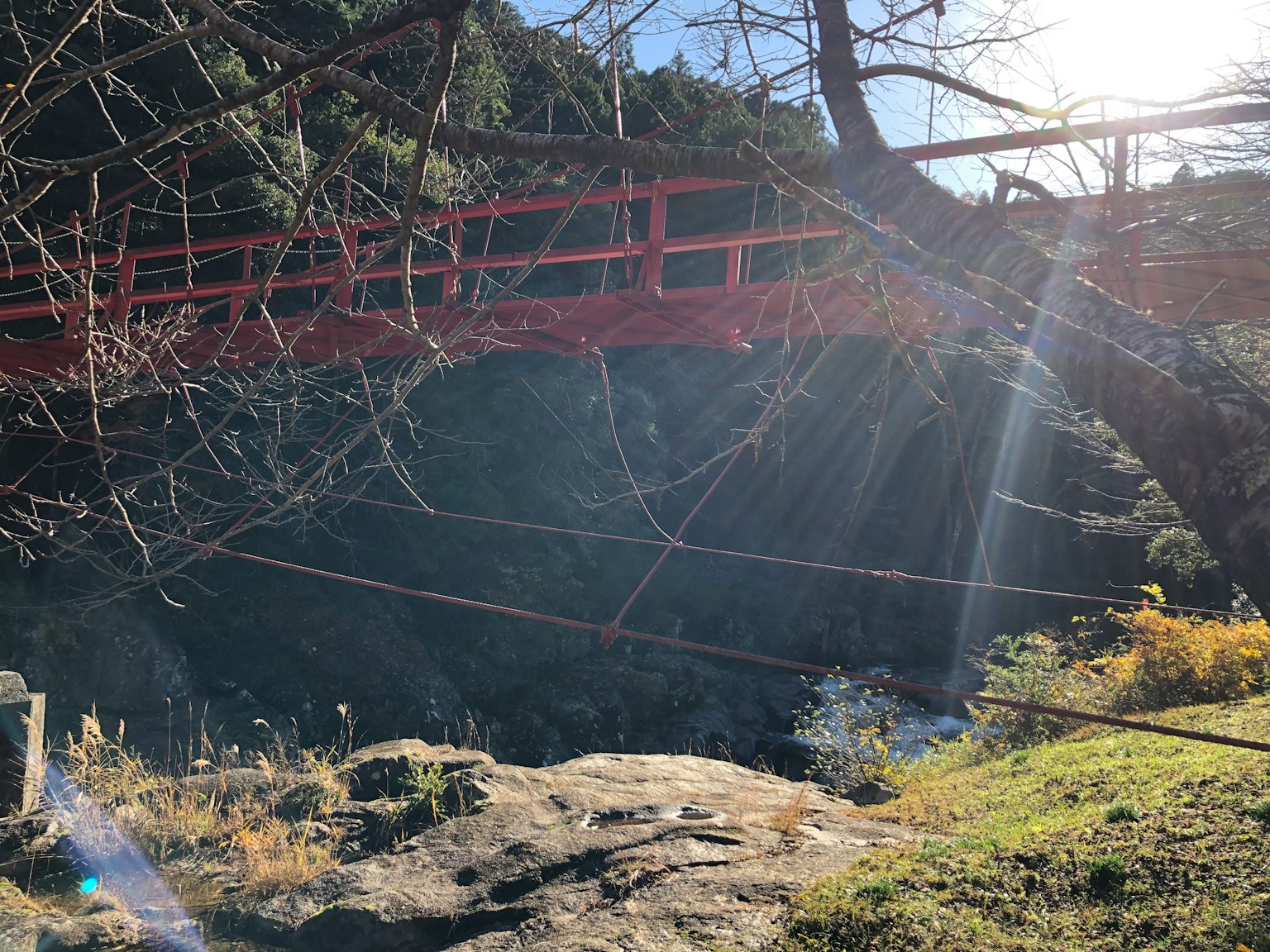Jembatan merah di atas pemandangan berbatu dengan sinar matahari menyinari pohon