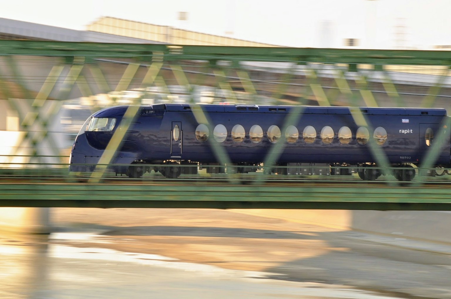 Blue Shinkansen train passing under a green bridge