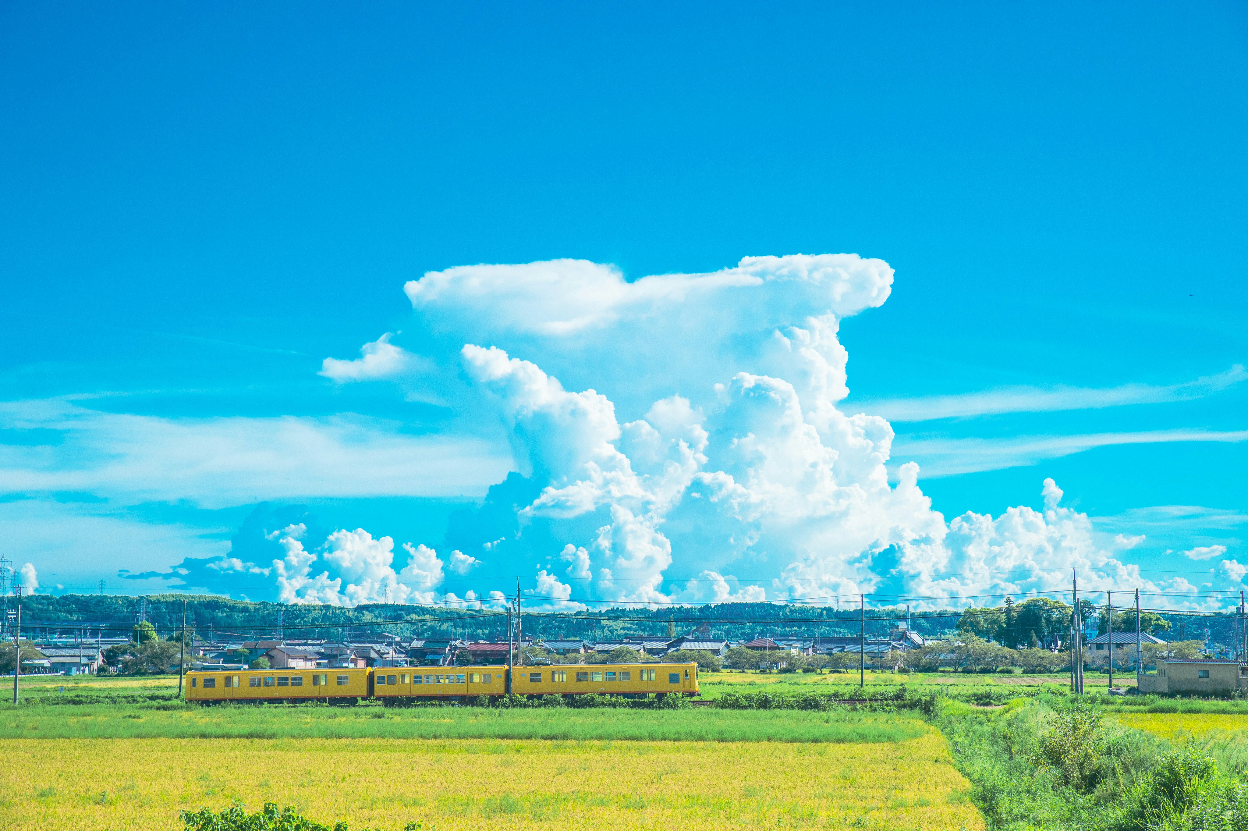 緑の草原を走る黄色い列車と青空の雲
