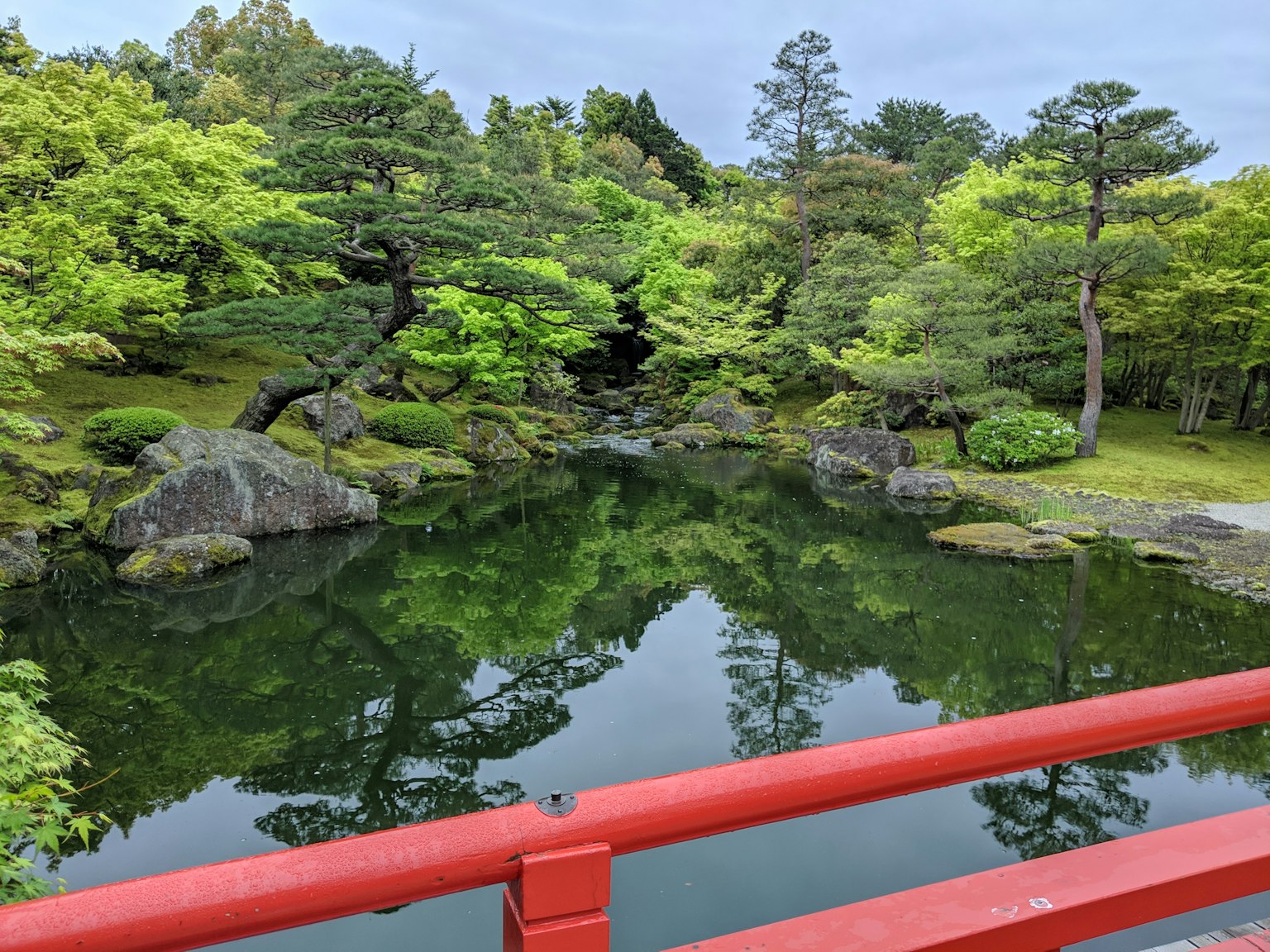 Photo of a pond reflecting greenery with a red bridge