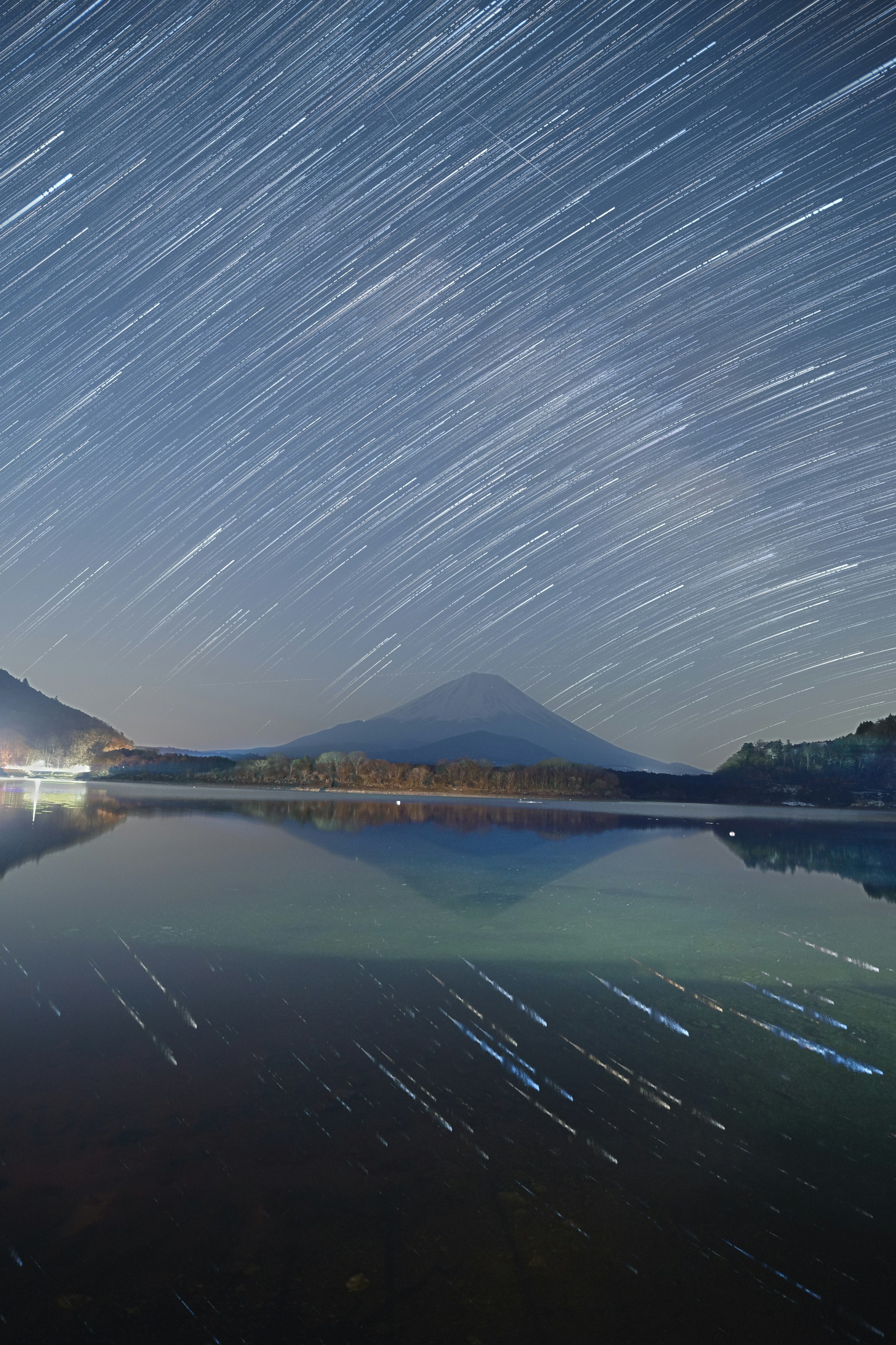 湖面に映る夜明け前の山並みと流れる星の軌跡