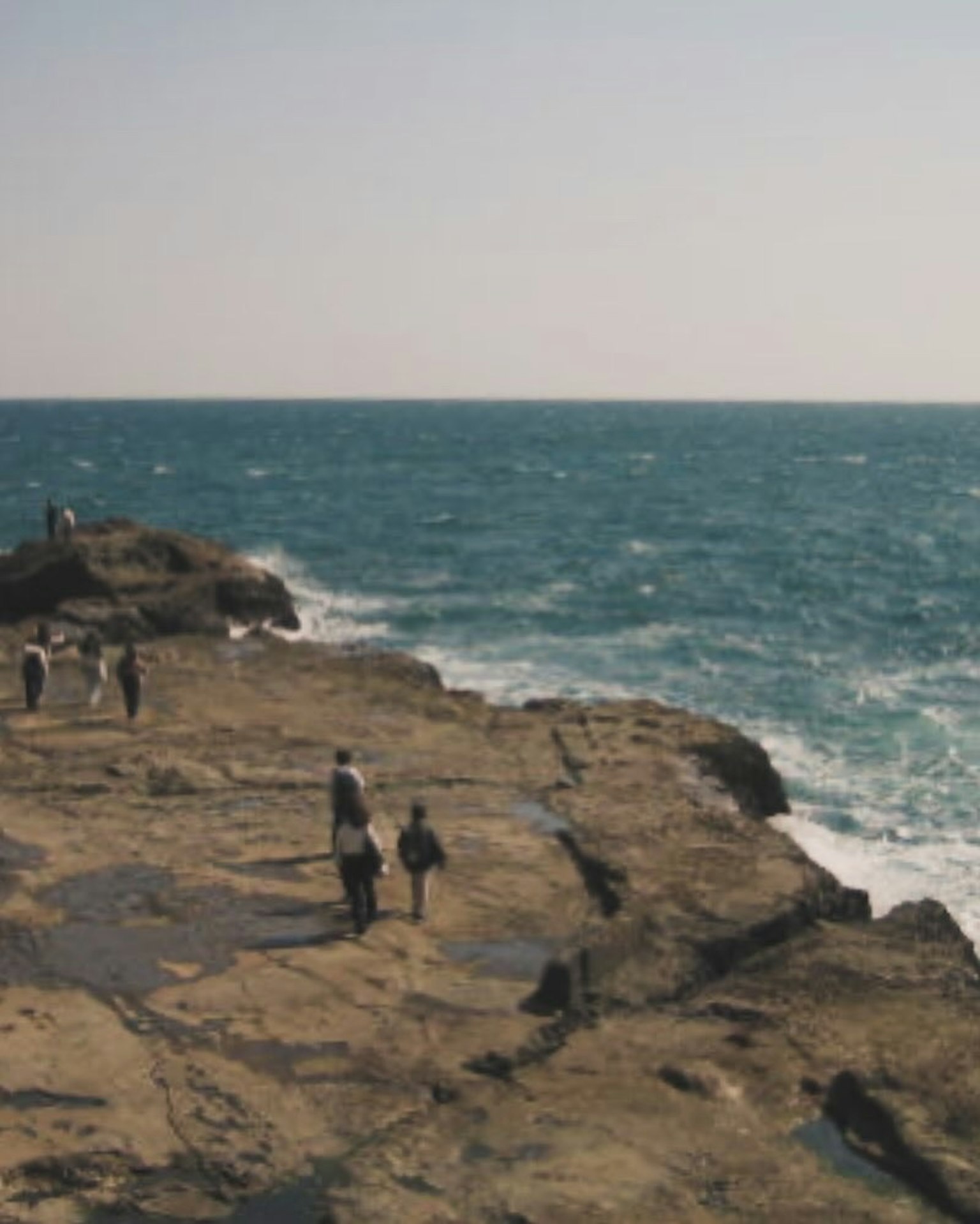 People standing on rocky shore with blue ocean