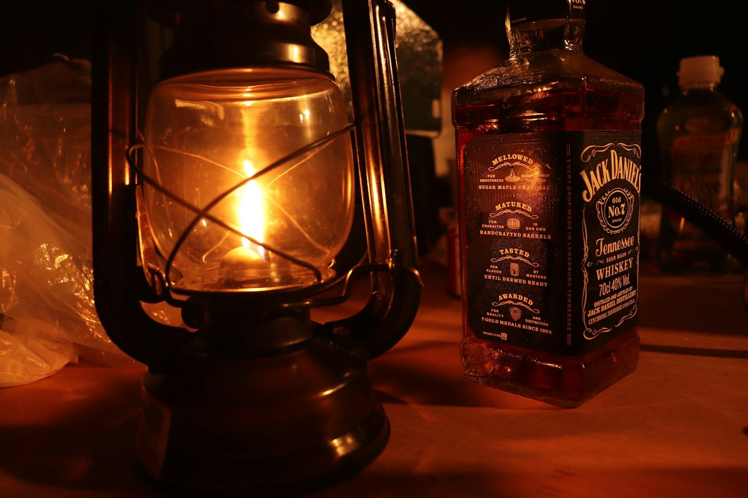 An oil lantern next to a whiskey bottle in a dimly lit setting