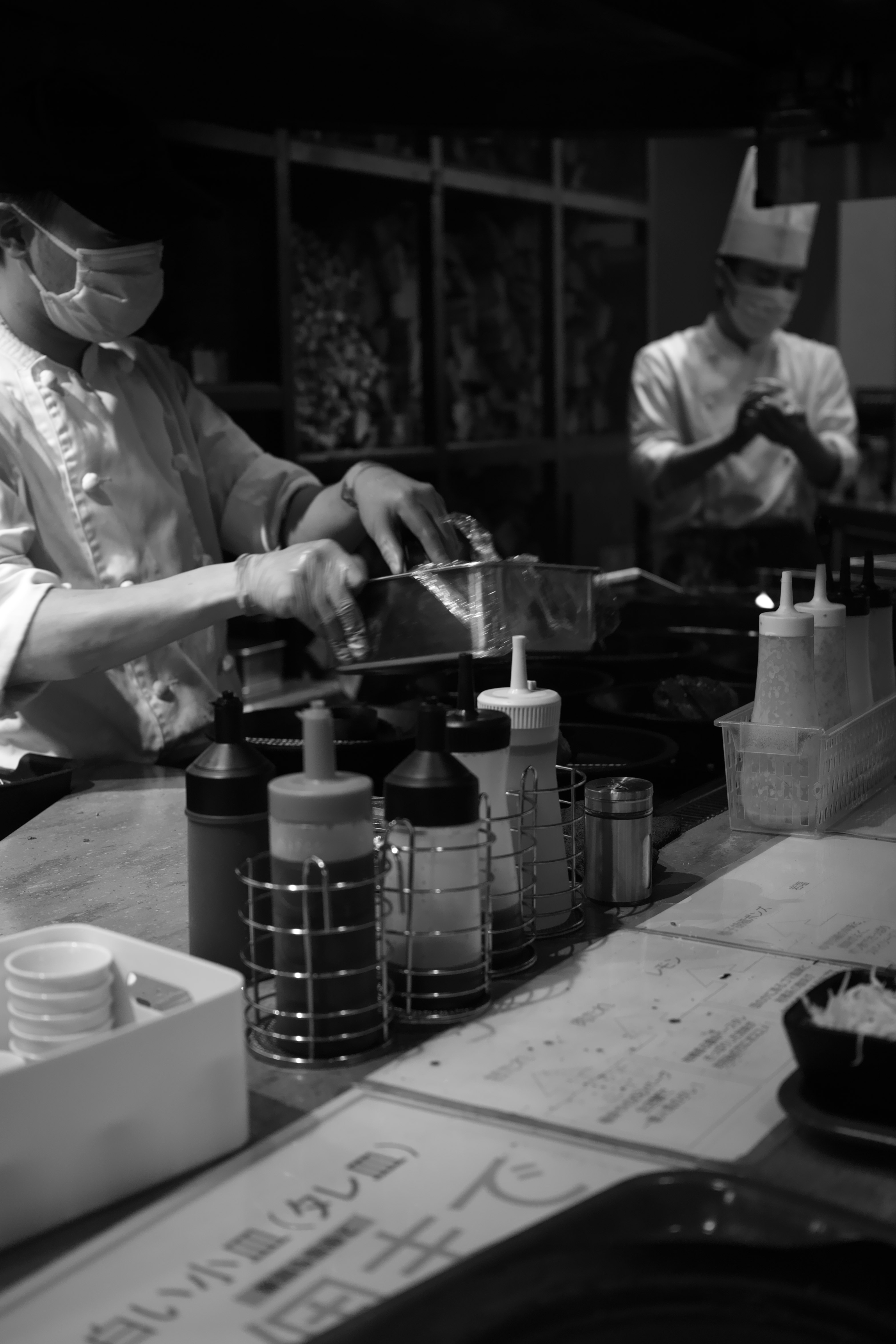 hands preparing food behind a counter with utensils and containers