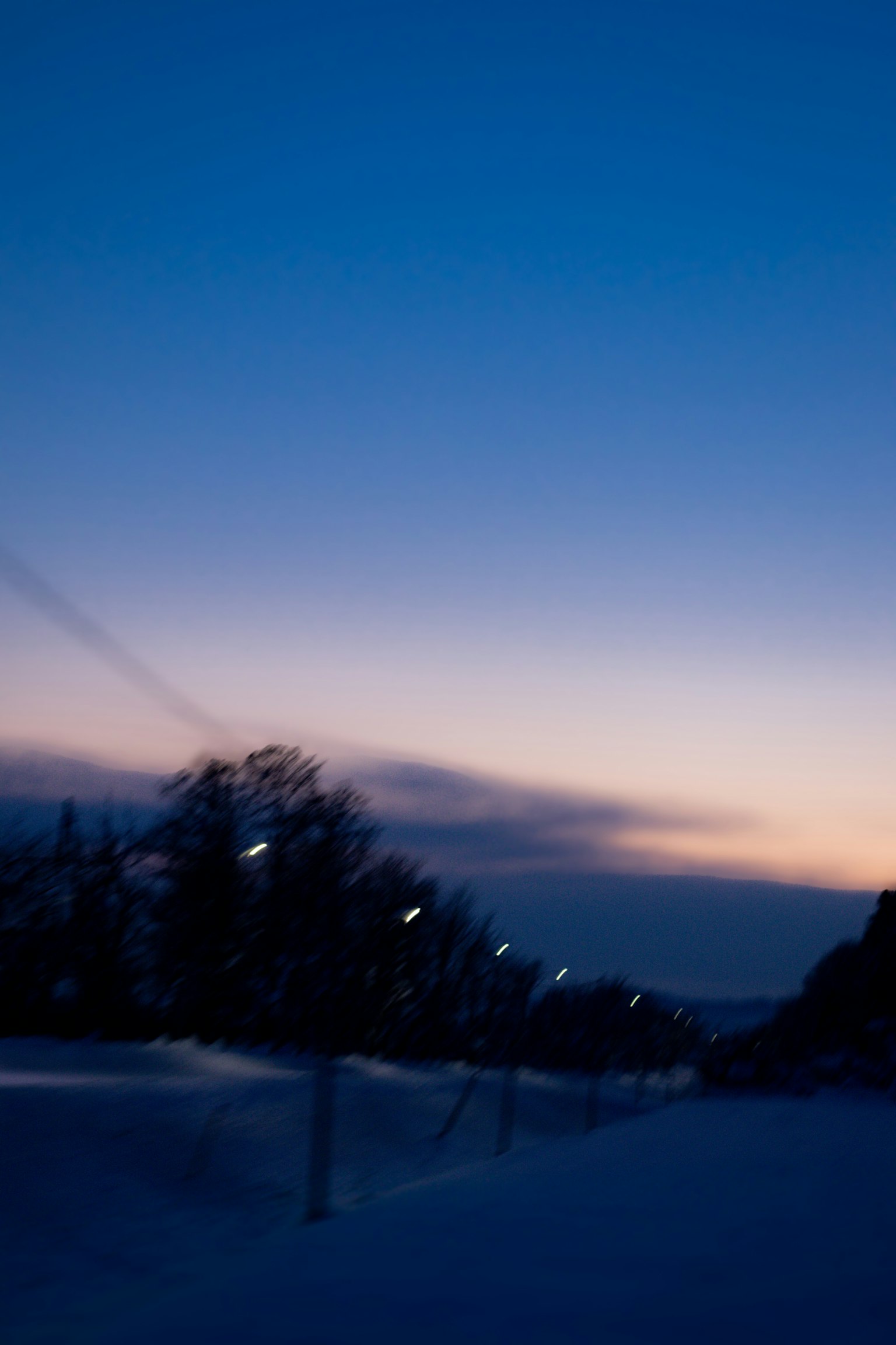 Winter twilight landscape with a blue sky and orange gradient streetlights lining a snowy path