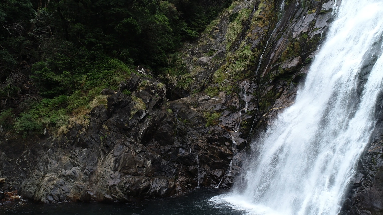 Schöne Naturlandschaft mit einem Wasserfall neben felsigen Klippen und üppigem Grün