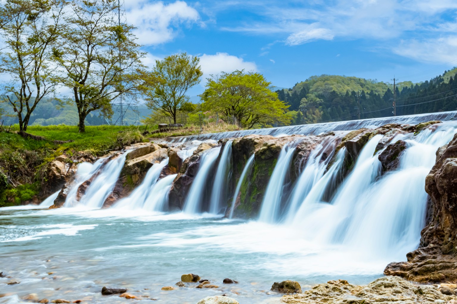 Khung cảnh đẹp với thác nước và dòng suối bao quanh bởi cây xanh và bầu trời xanh