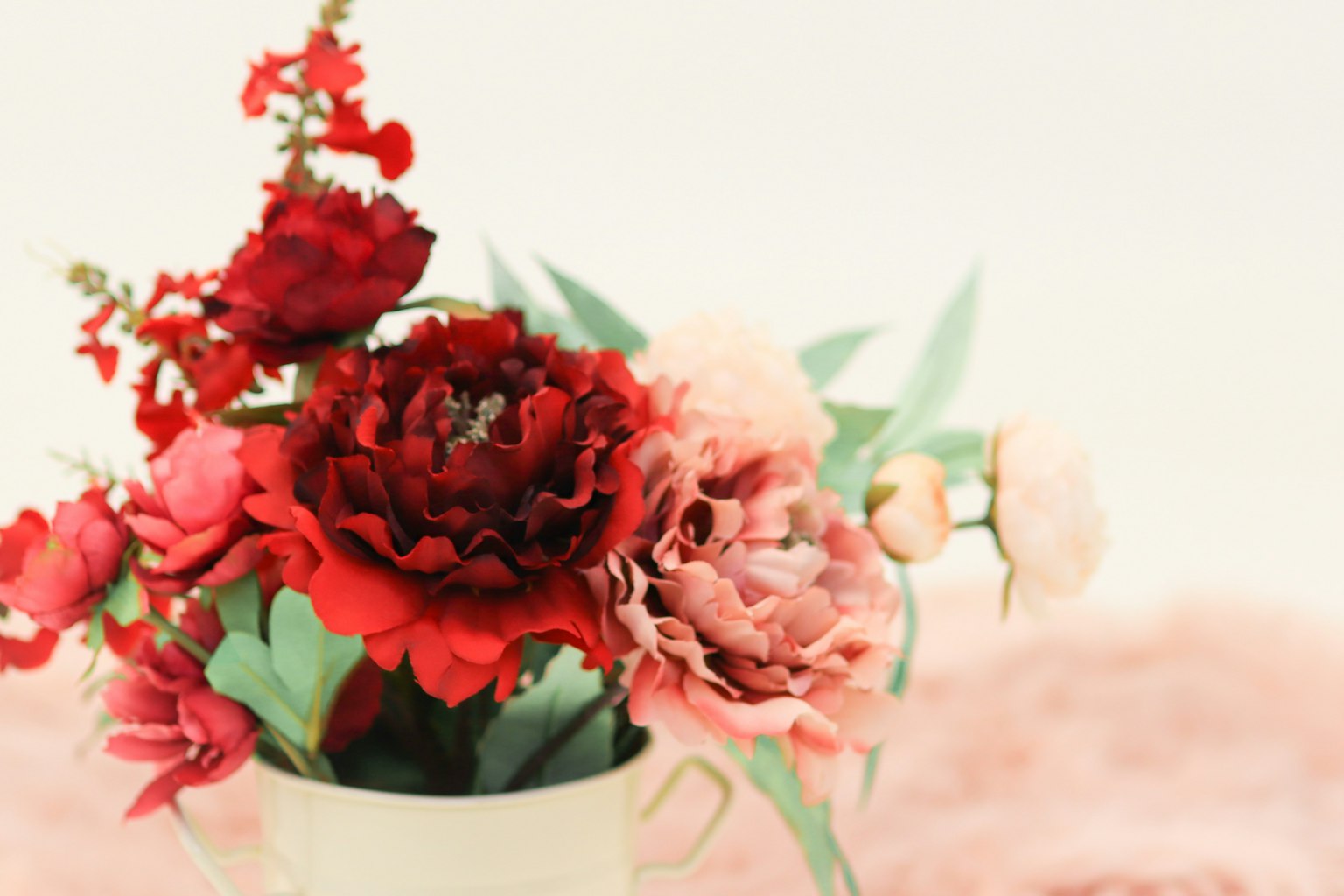 Arrangement aus roten und rosa Blumen in einer weißen Vase auf einem sanften Hintergrund