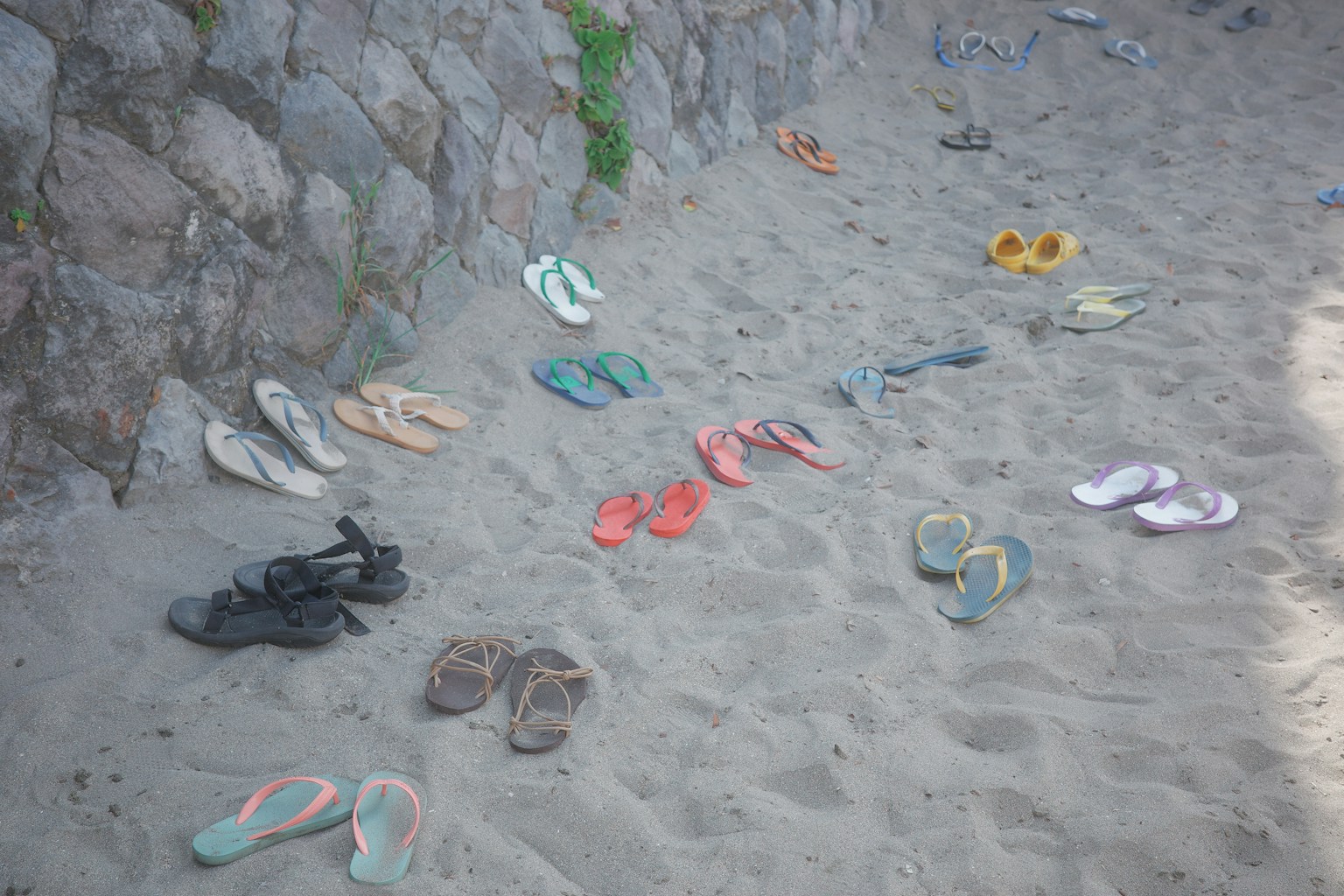 Various sandals and flip-flops scattered on the sandy beach