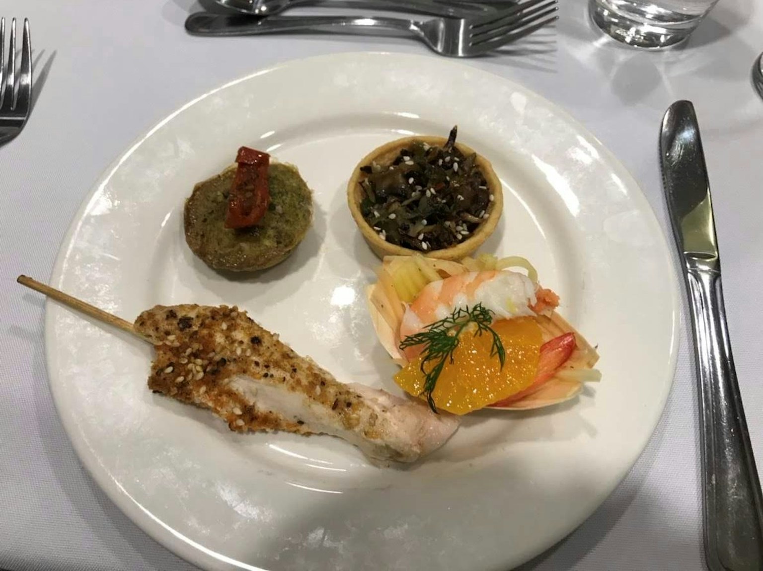 Plato con brocheta de pollo a la parrilla, pasta verde, ensalada de mariscos y ensalada de verduras negras