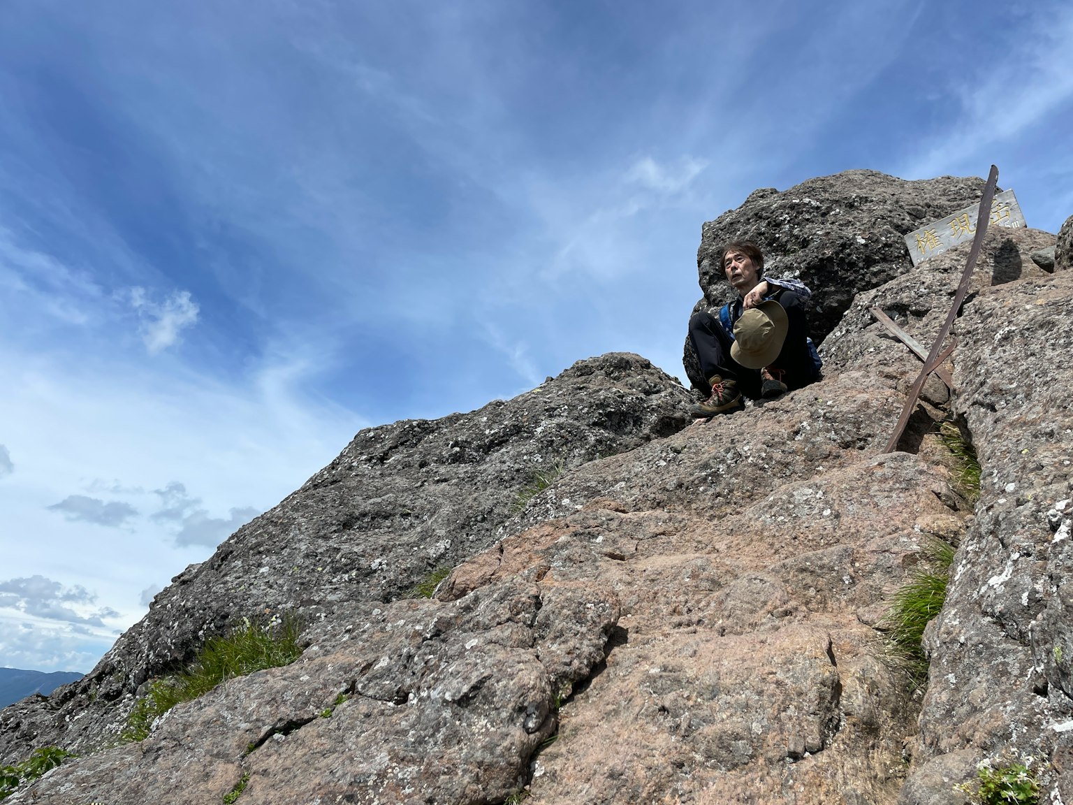 Persona sentada en una montaña rocosa con fondo de cielo azul