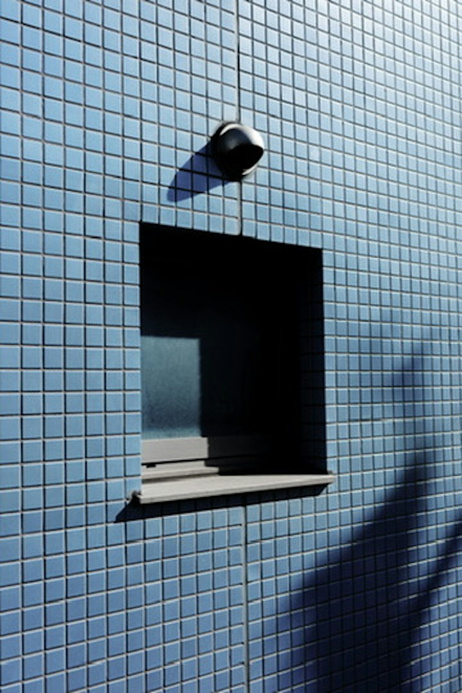 Black window on a blue tiled wall with a security camera