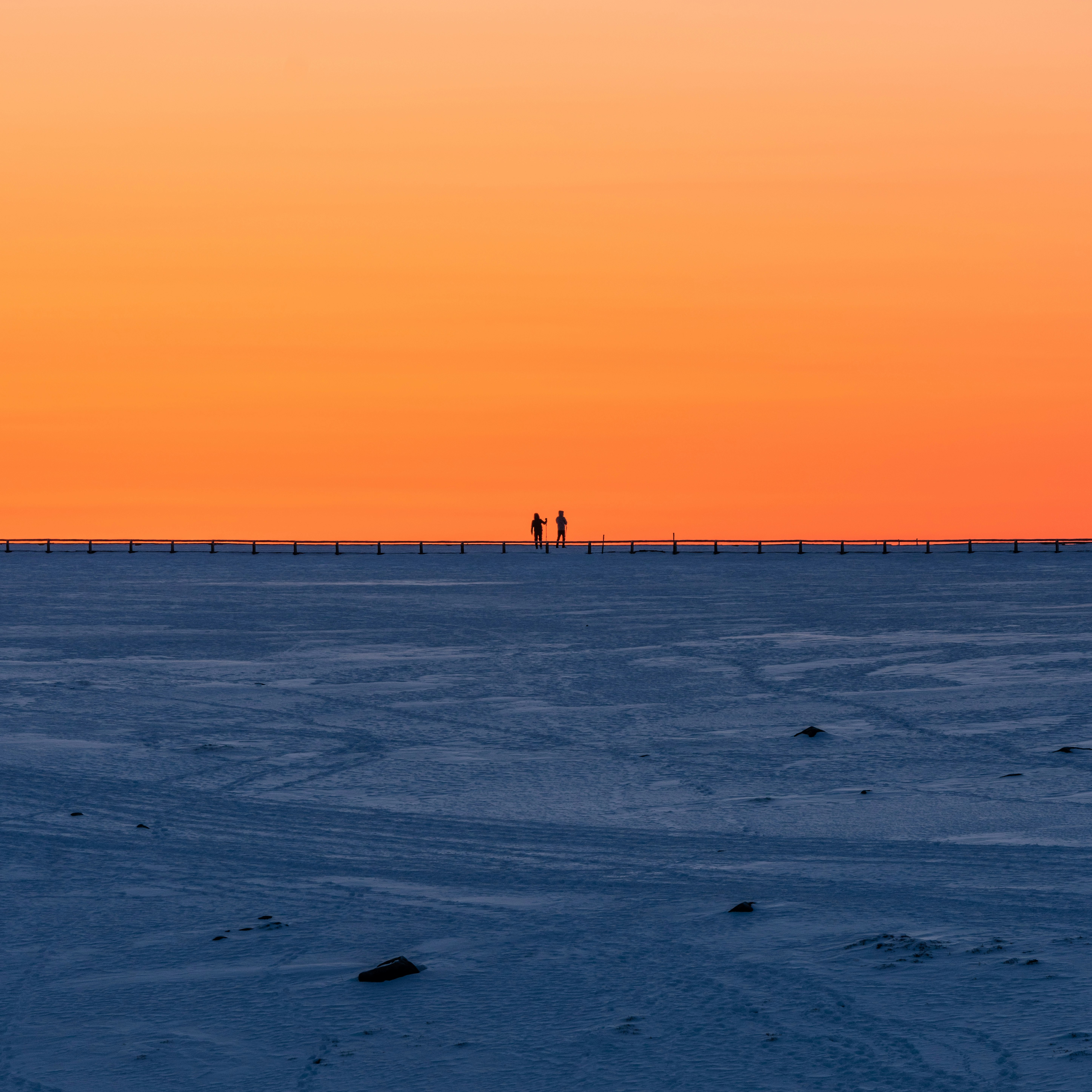 Cielo de atardecer sobre una amplia playa de arena, siluetas de personas caminando a lo lejos