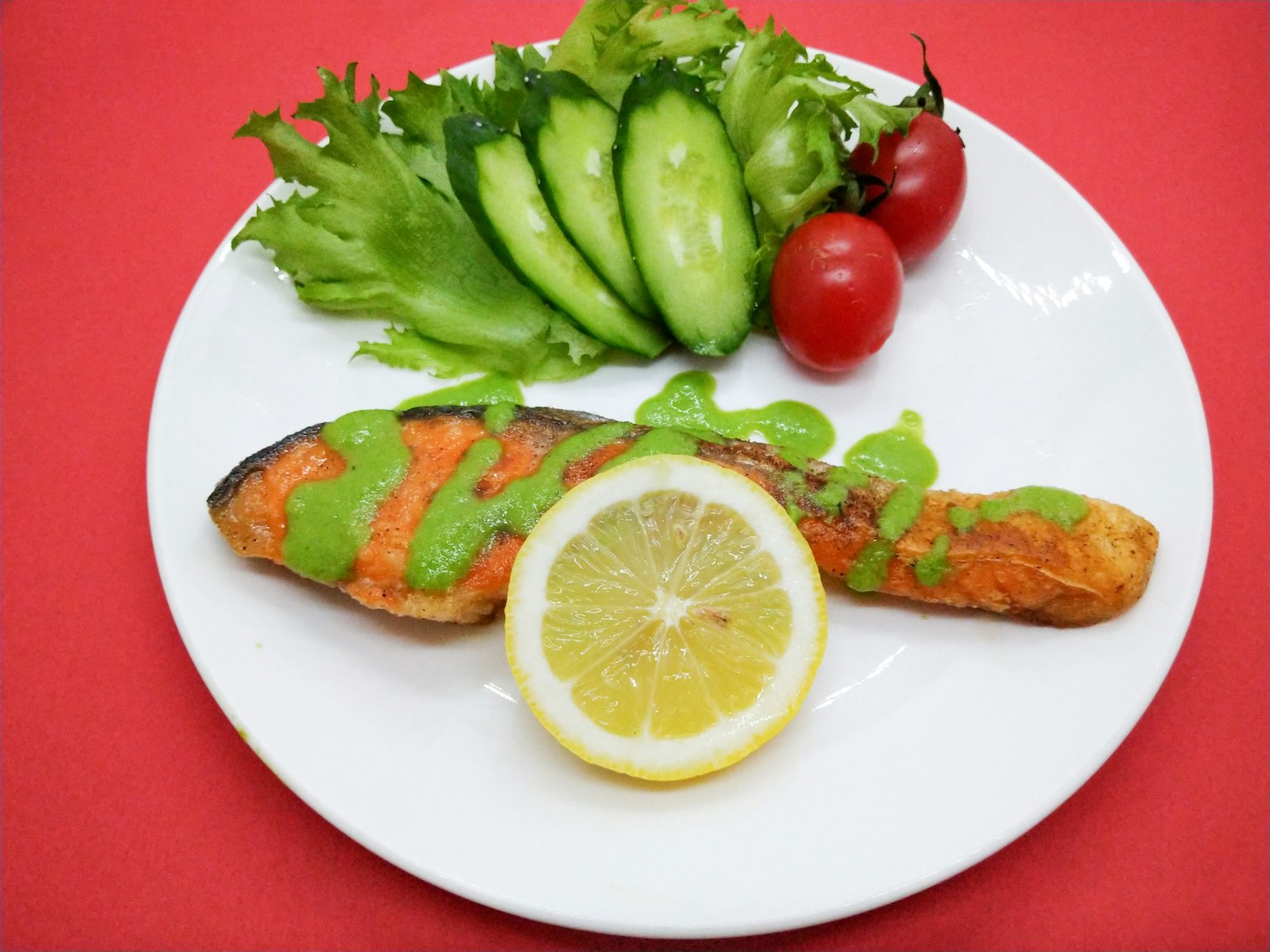 Salmone alla griglia su un piatto bianco con fette di limone e insalata fresca con cetrioli e pomodorini