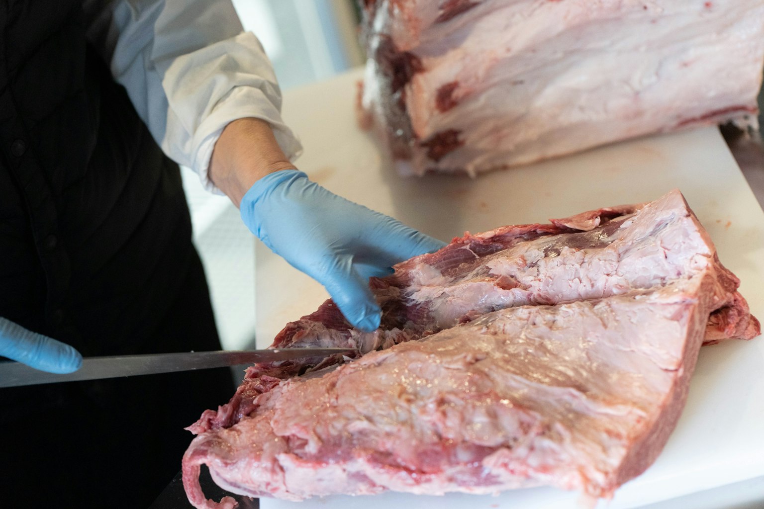 Close-up of a butcher's hand wearing blue gloves cutting a large piece of meat