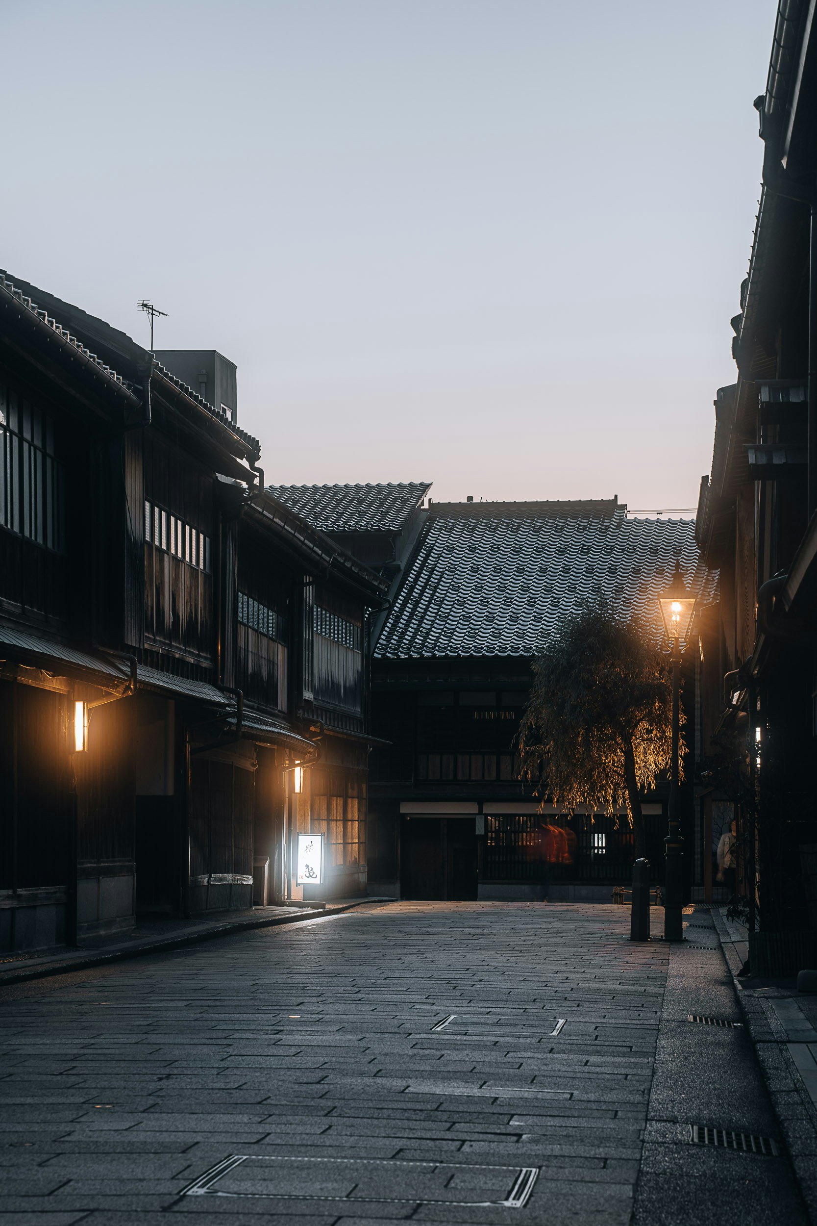 夕暮れの路地に並ぶ町家と街灯