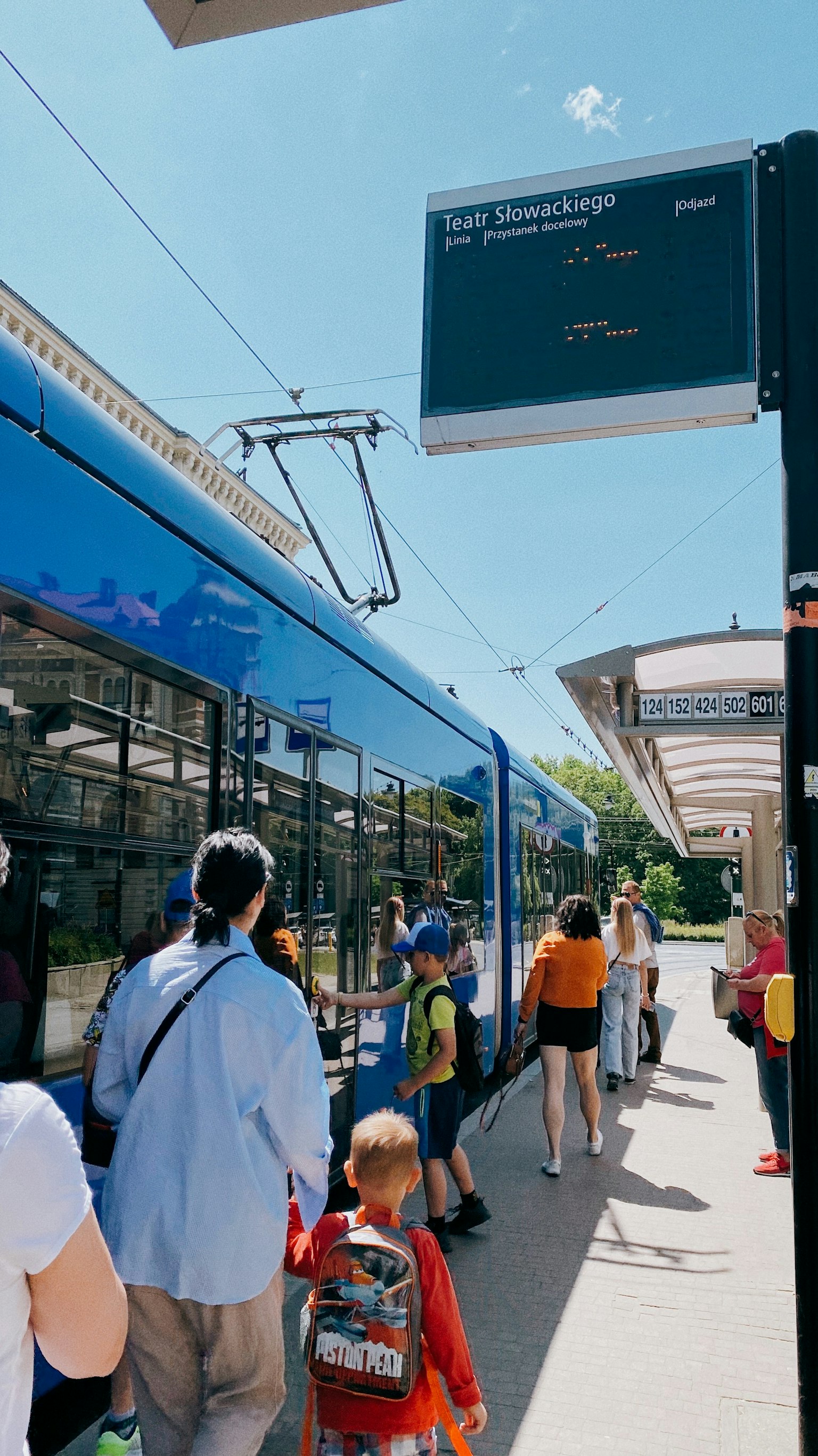 在藍色電車和數位顯示板旁等候的人們