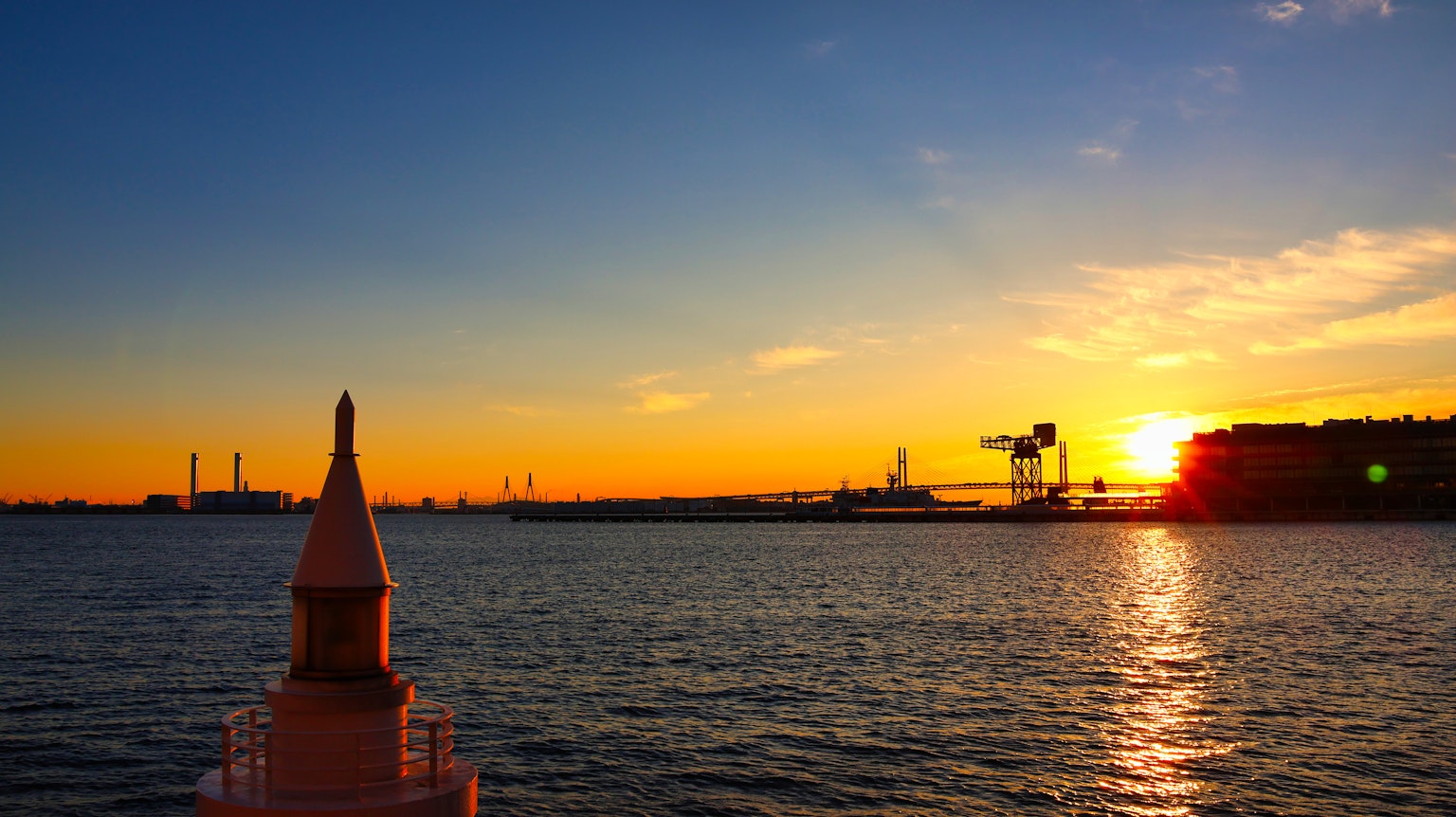 Panoramablick auf den Sonnenuntergang über dem Wasser mit Hafenkränen im Hintergrund