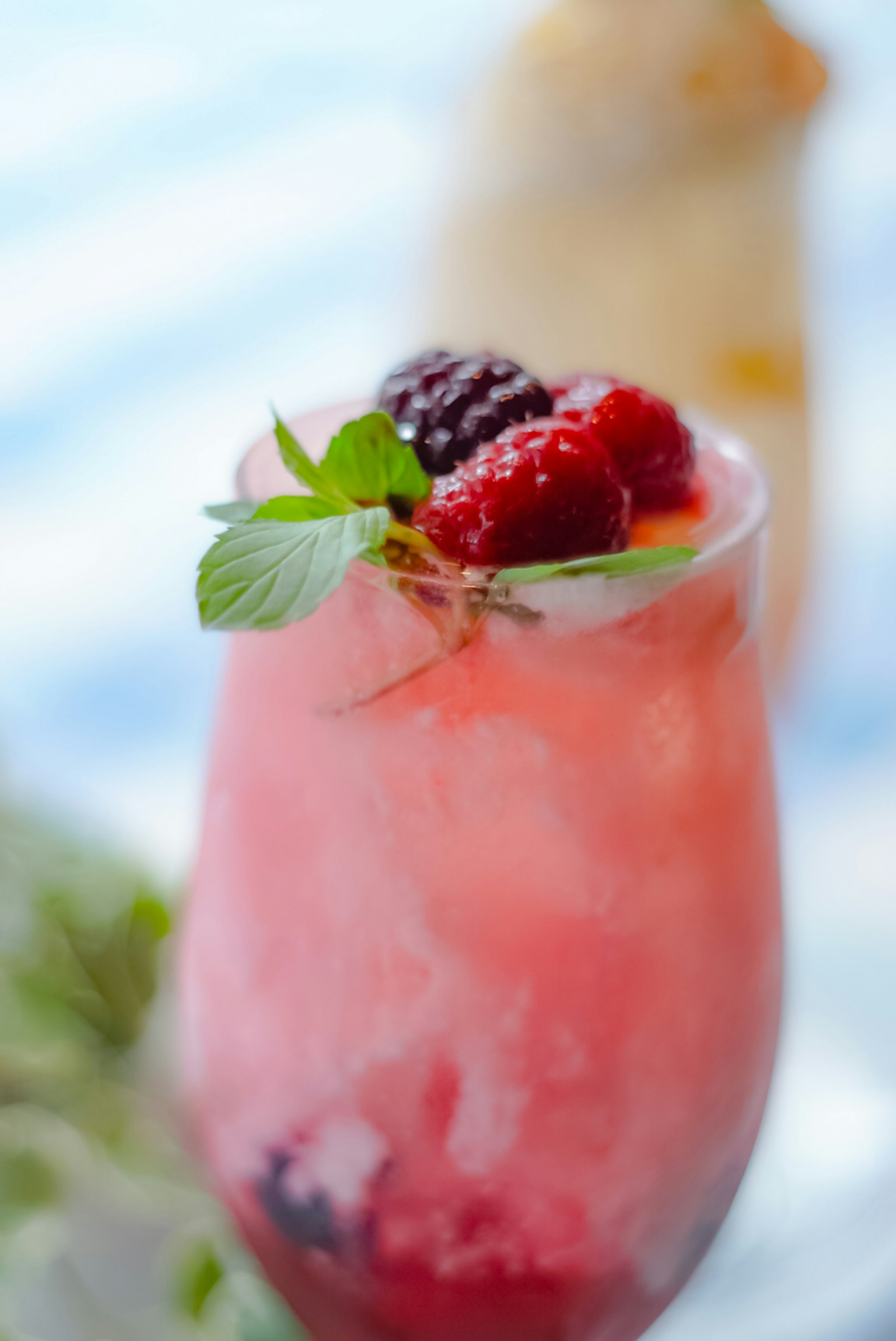 Un vaso de cóctel lleno de una bebida de frutas rojas adornado con hojas de menta