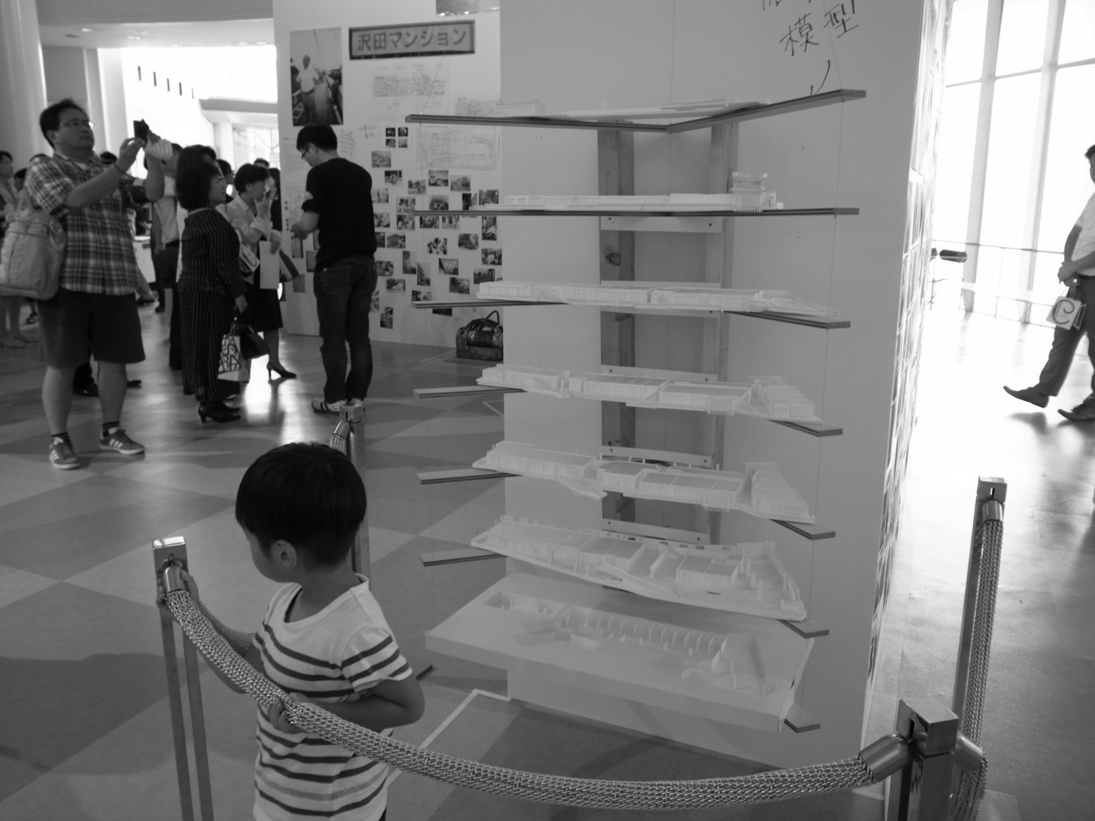 一个孩子在黑白展览空间中观察一个白色的架子结构，背景有一些人