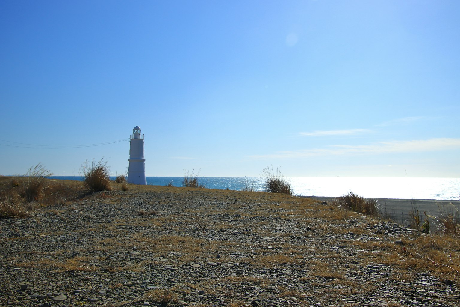 Ein Leuchtturm steht unter einem blauen Himmel mit ruhigem Meer