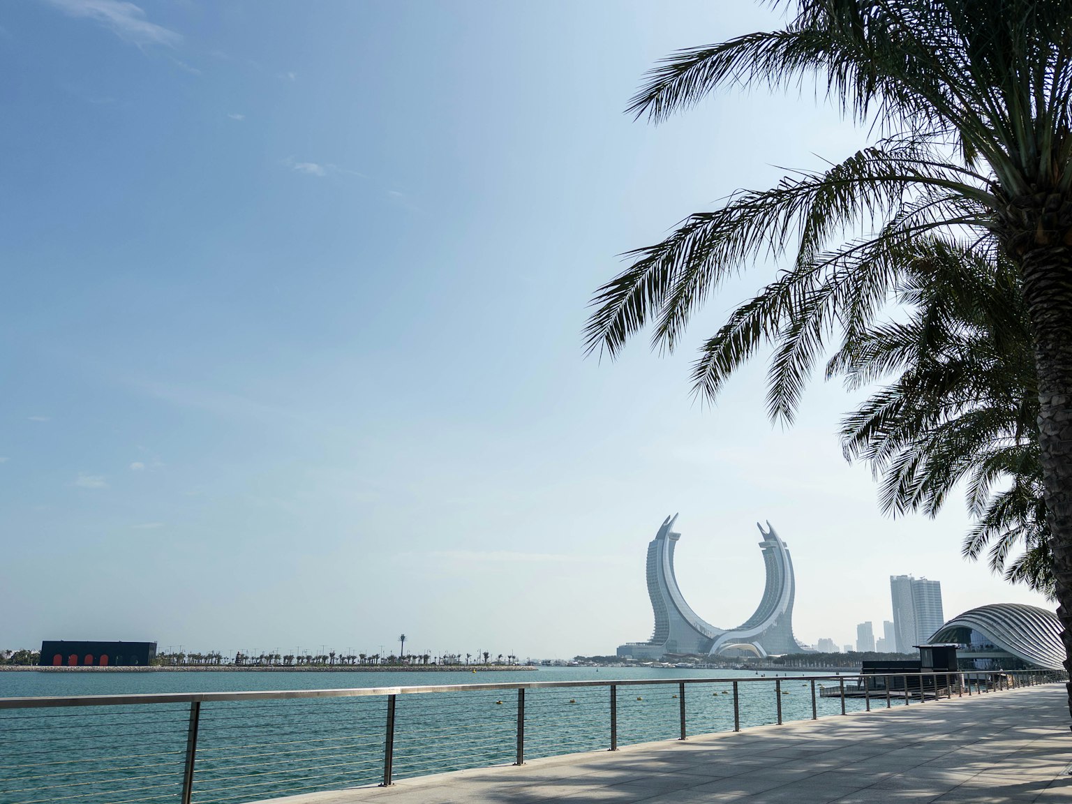 Vista panoramica con palme e una struttura architettonica unica lungo la riva