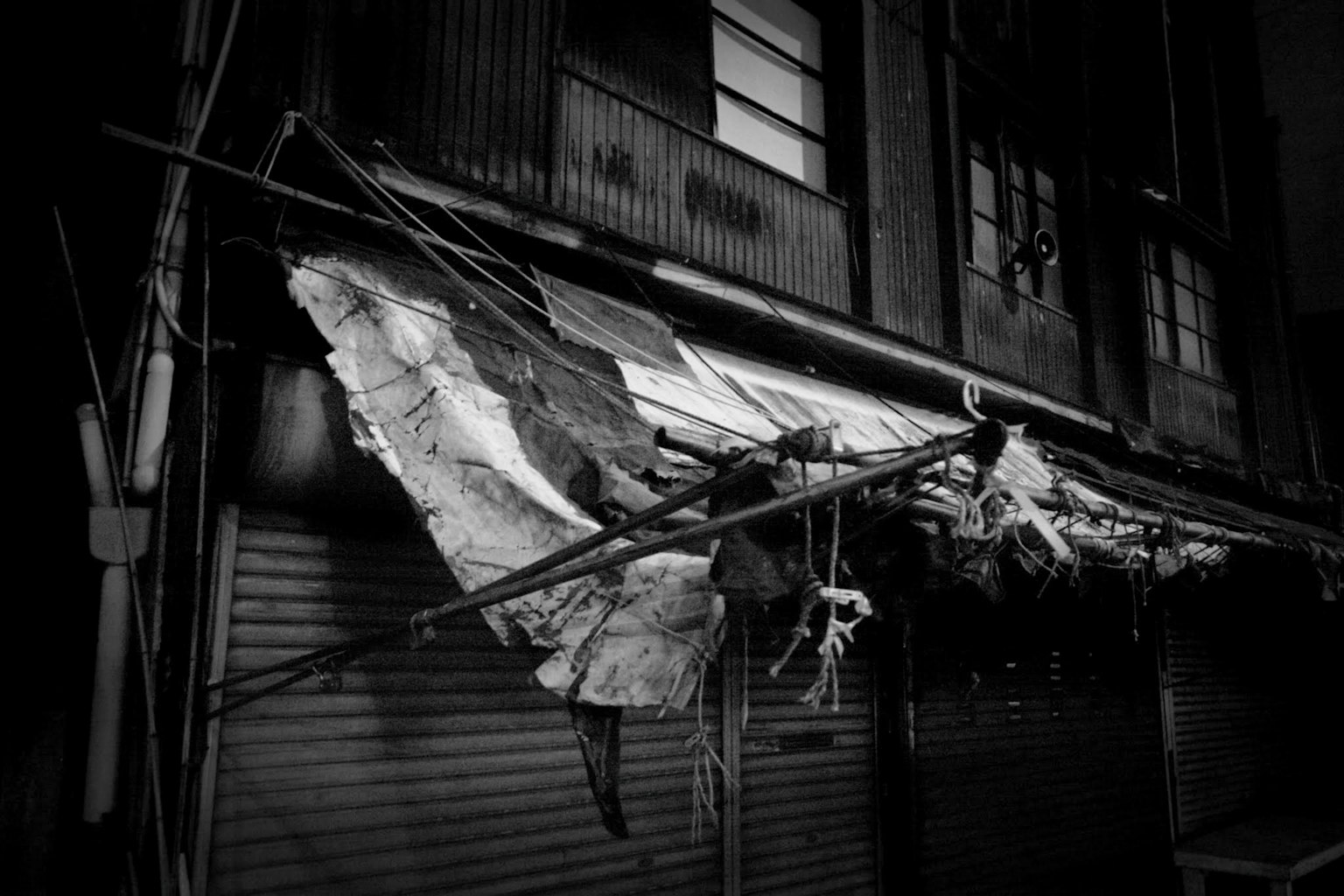 Tattered fabric and metal structure hanging in a dim alley