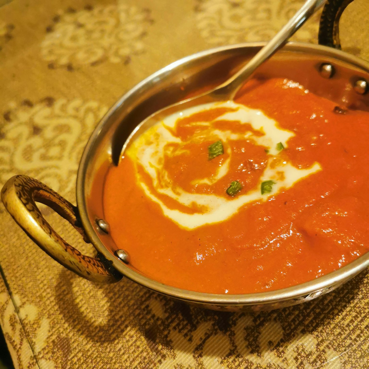 Curry di pomodoro cremoso in una ciotola d'argento con una spirale di panna
