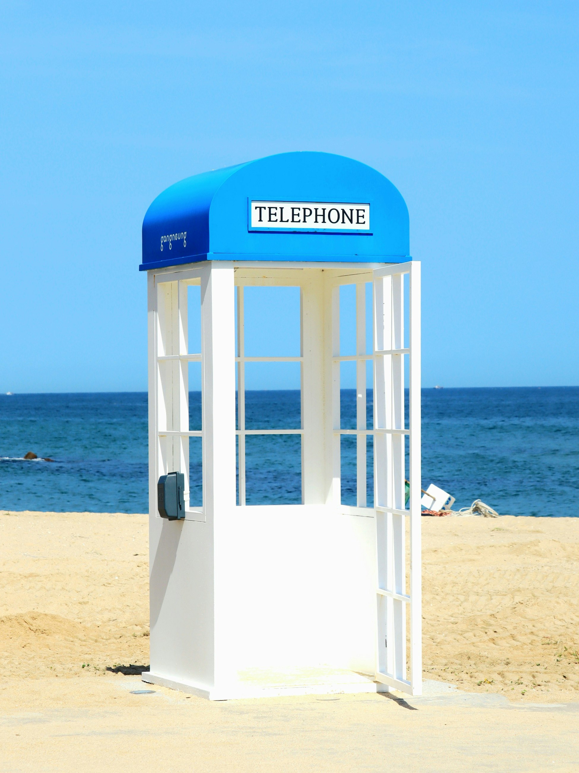 青空の下の海辺にある白い電話ボックス