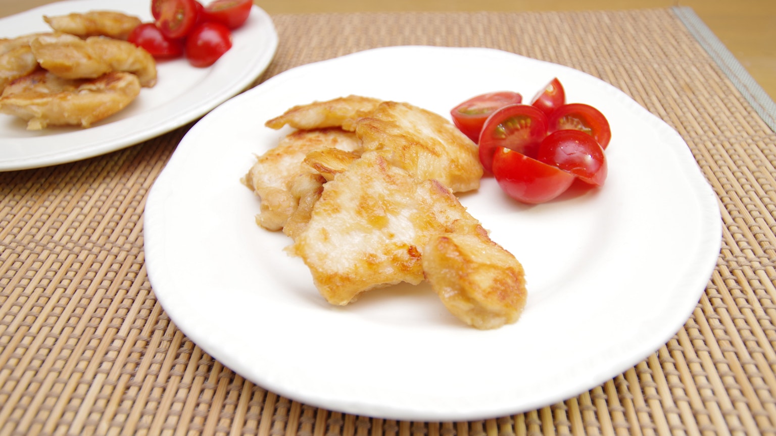Frittierte Hühnerstücke auf einem weißen Teller mit Kirschtomaten serviert