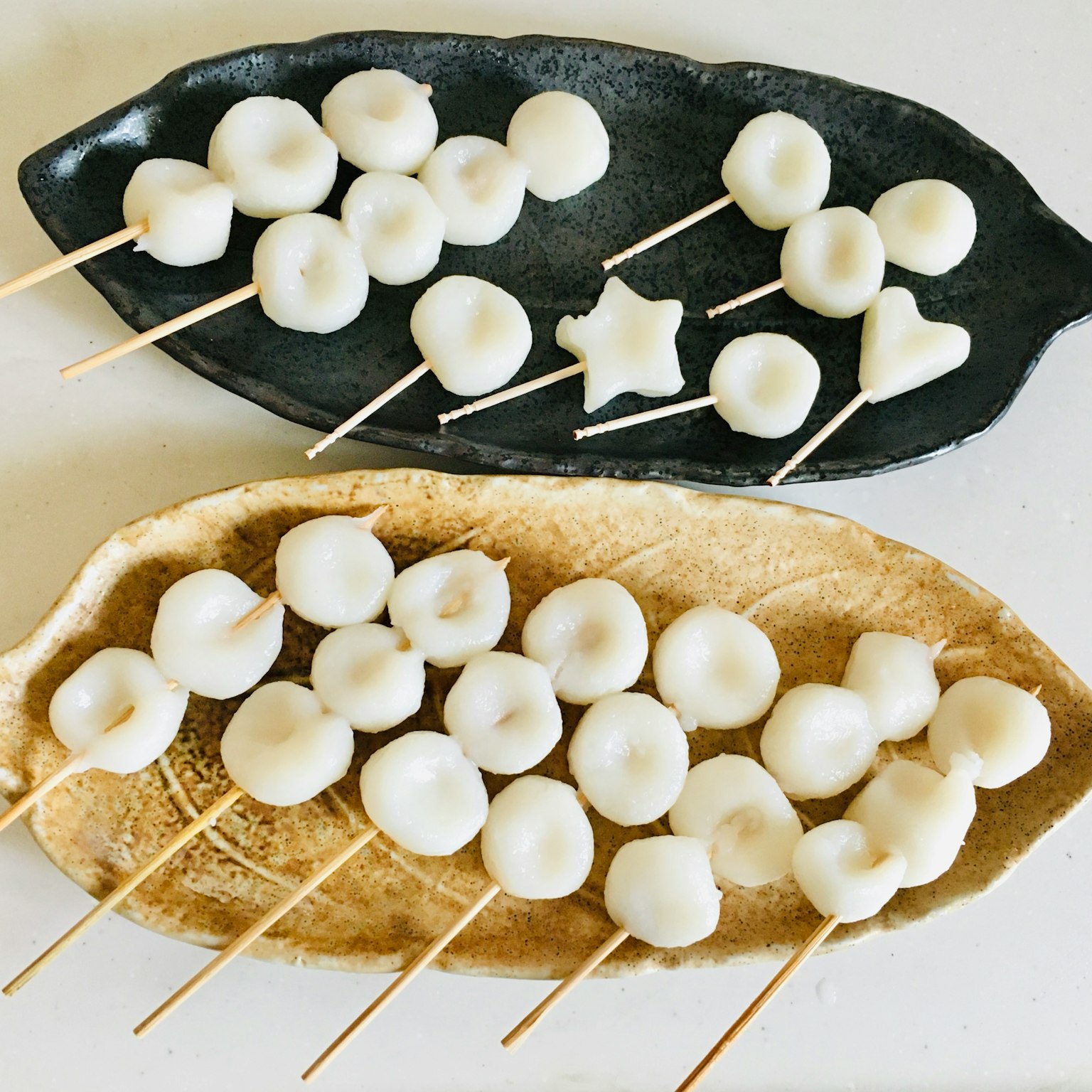 Two plates with white dumplings on skewers in various shapes