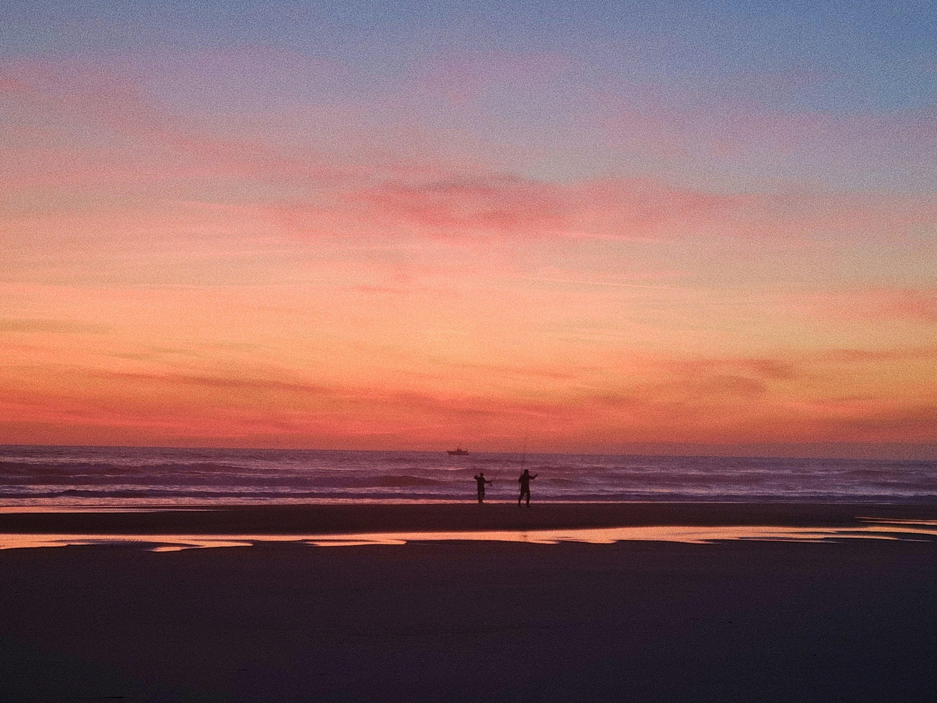夕焼けの海辺で砂浜を歩く人影のある風景