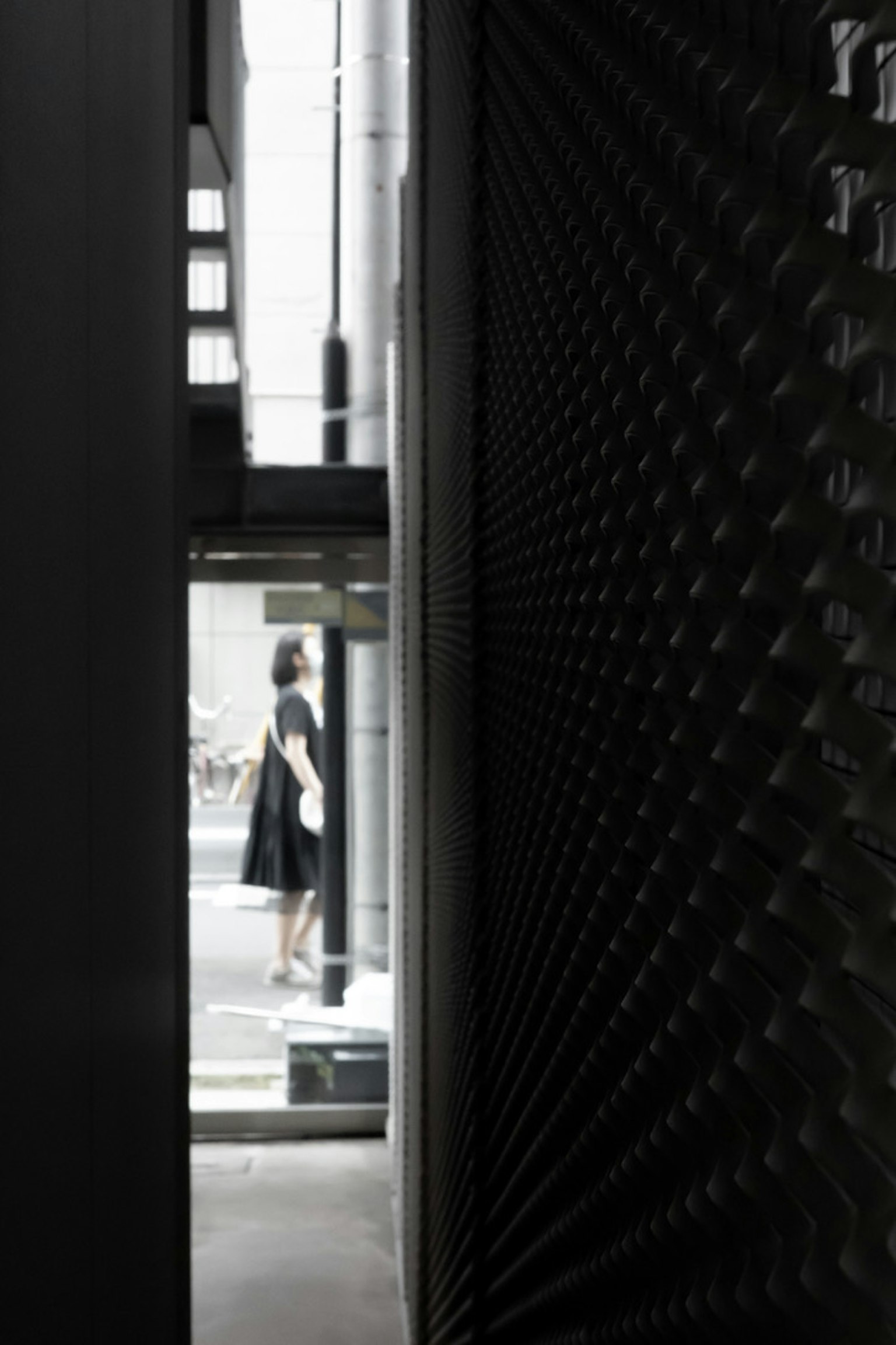 A view of a woman standing in a city through a narrow gap between dark walls