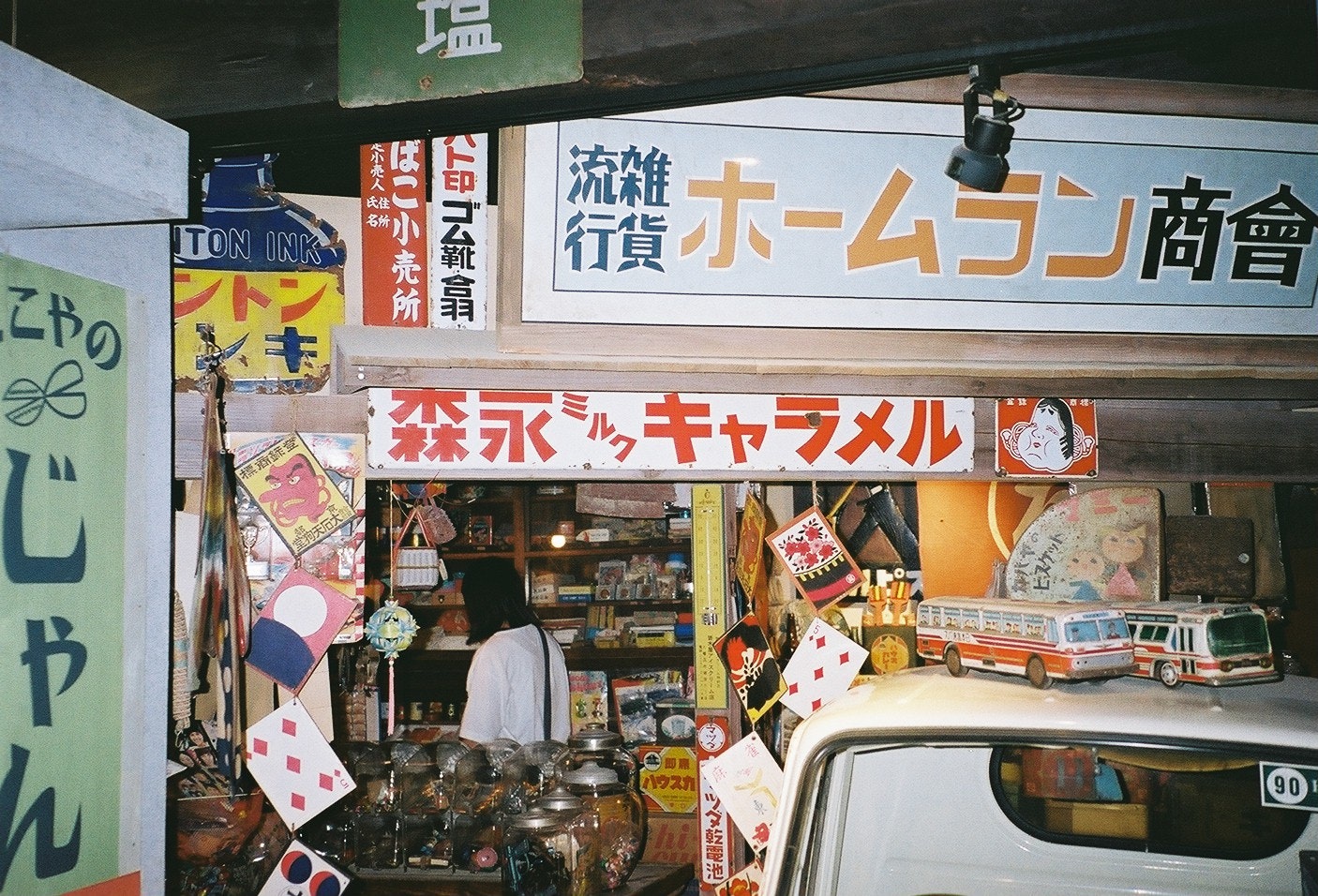 商店街店铺门面，招牌与杂货陈列、停着的汽车